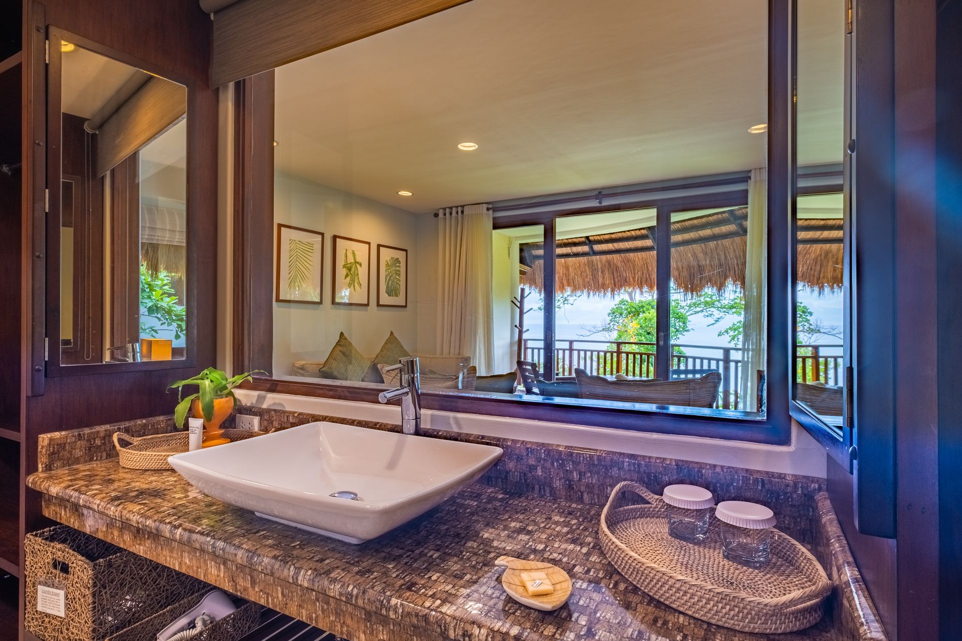 Granite bathroom vanity with vessel sink, candle, and mirror reflecting a tropical balcony view