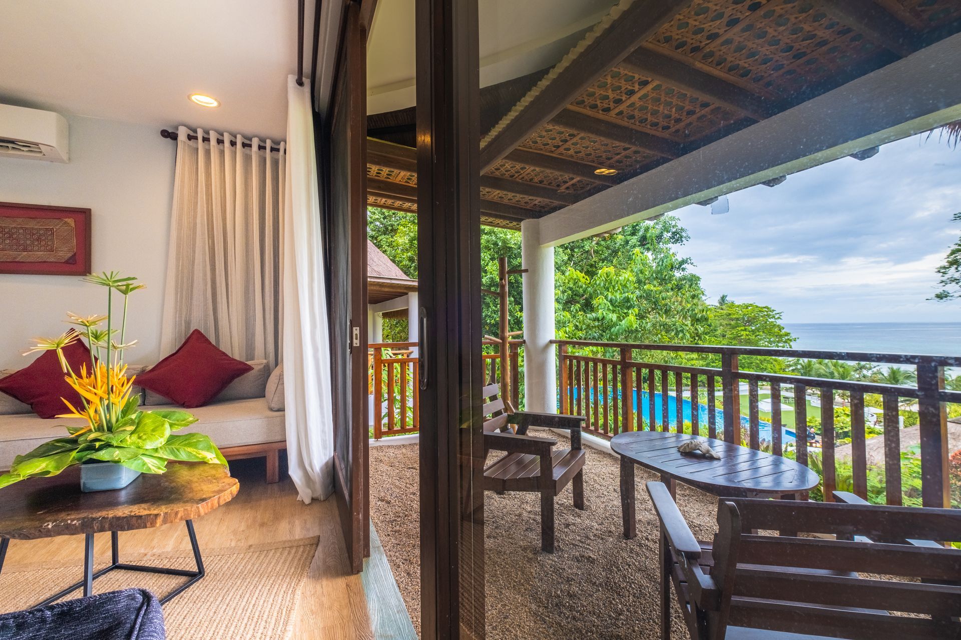 Cozy balcony seating with ocean view, wooden table, chairs, and tropical greenery beyond