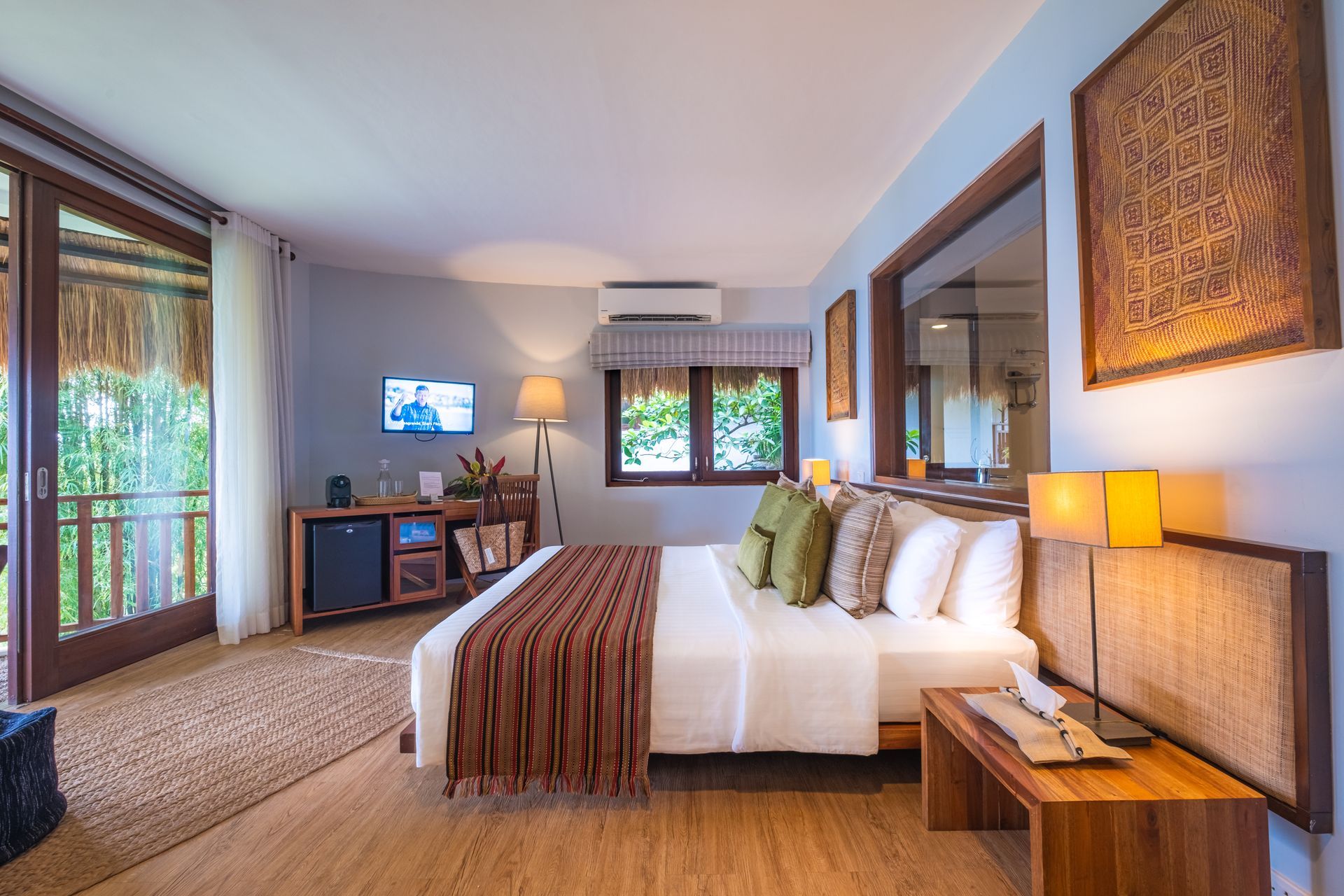 Bright hotel bedroom with a large bed, wooden accents, and a balcony view to the left