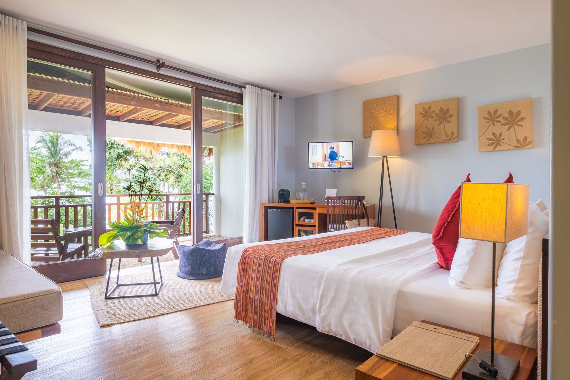 Bright hotel room with king bed, balcony view, desk, and warm decor
