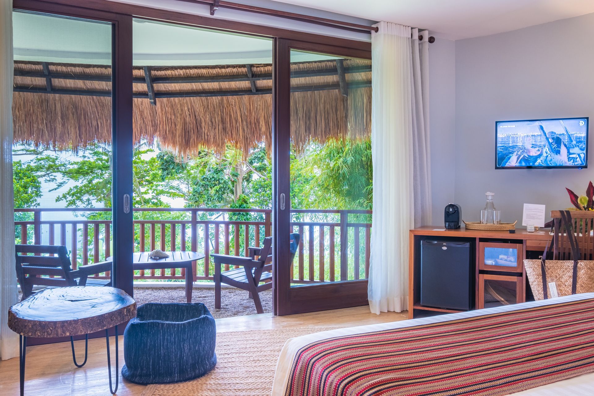 Cozy tropical bedroom with sliding doors to a balcony, TV on the wall, and striped bedspread