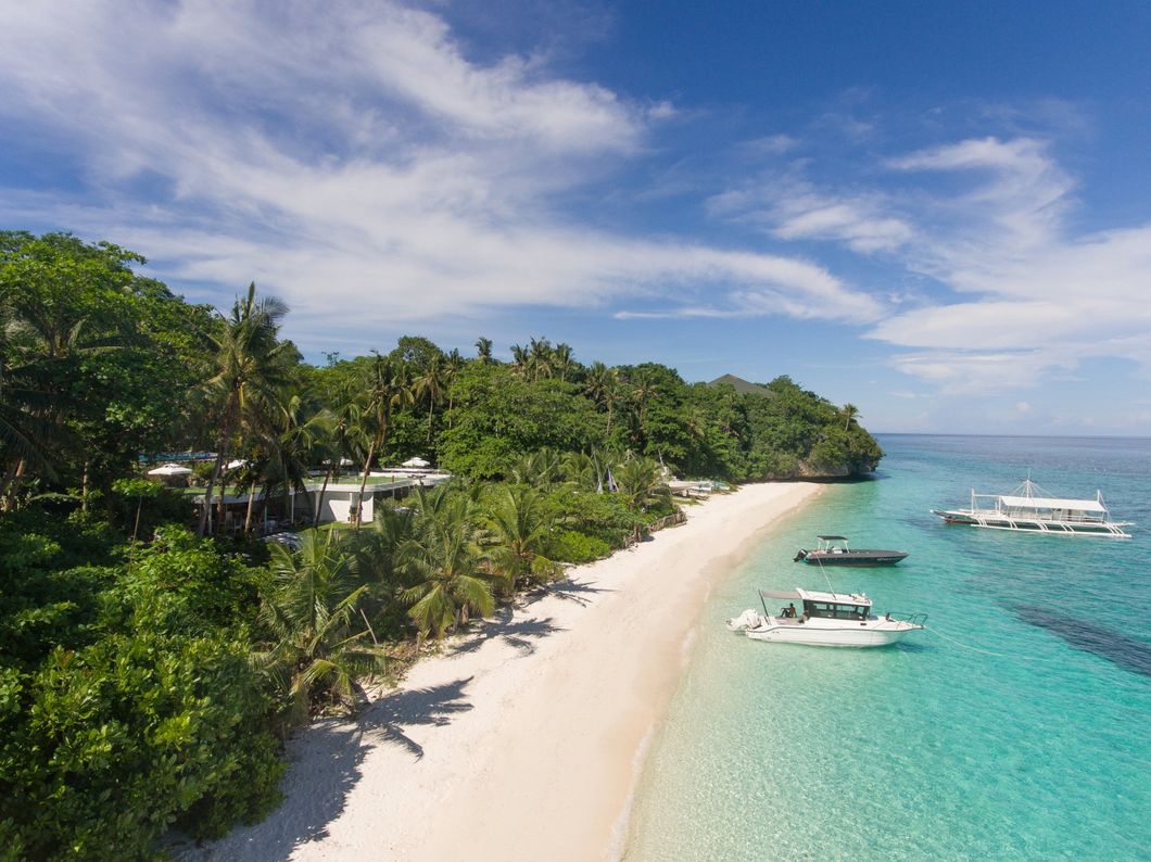 Tropical beach with white sand, turquoise water, palm trees, and anchored boats under a blue sky