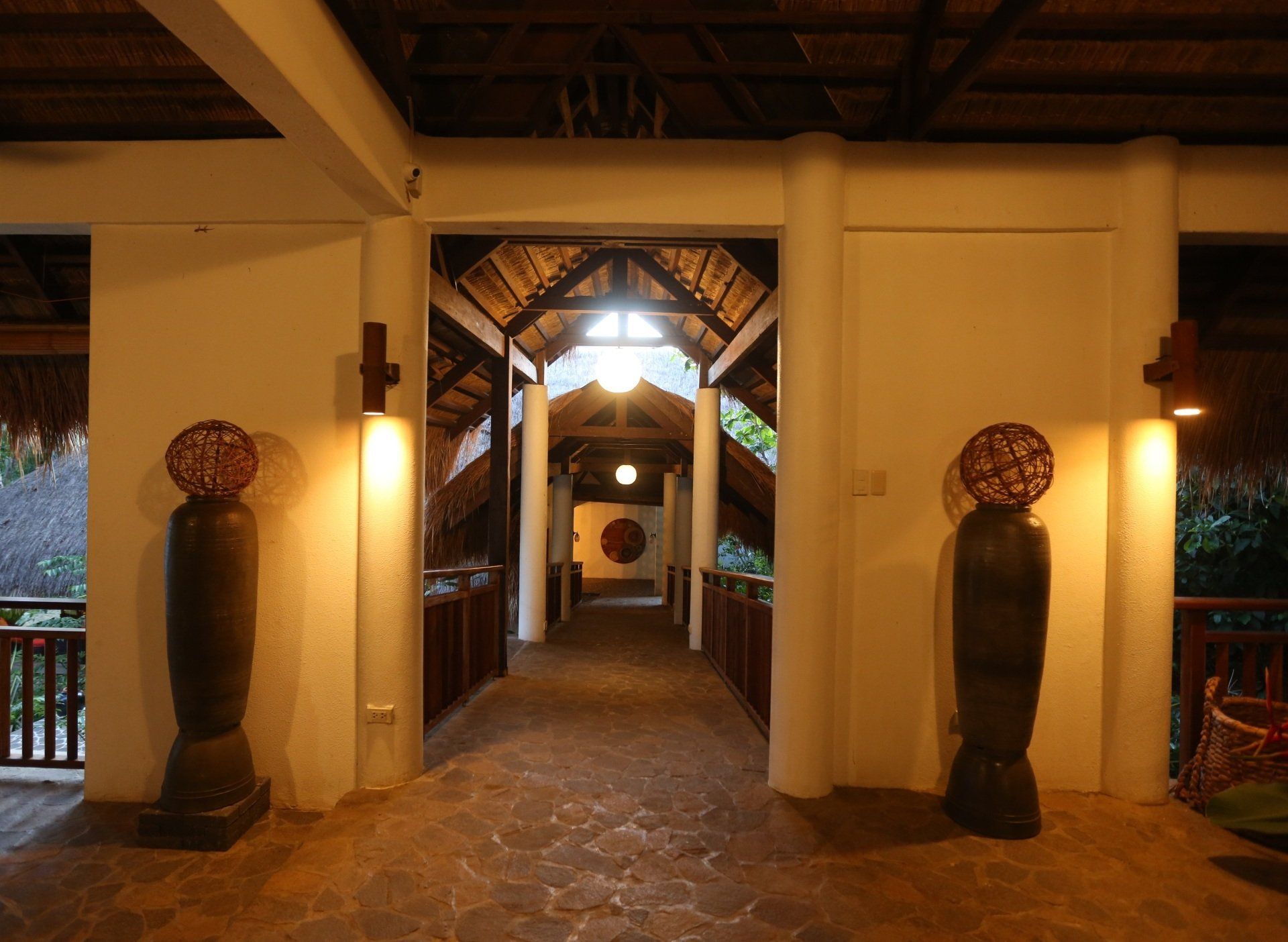 Warmly lit resort hallway with stone floor, wooden archway, and tall decorative vases at the entrance