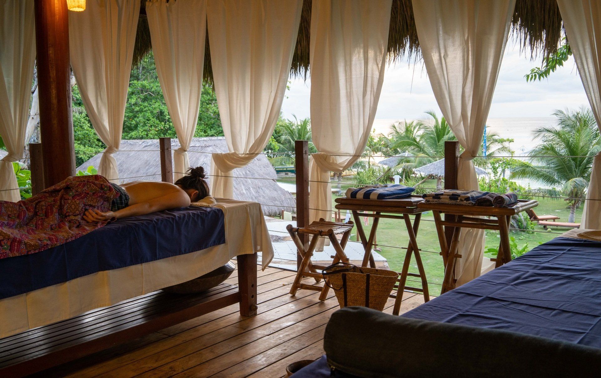 Open-air spa room with two massage beds, wooden deck, and tropical garden view