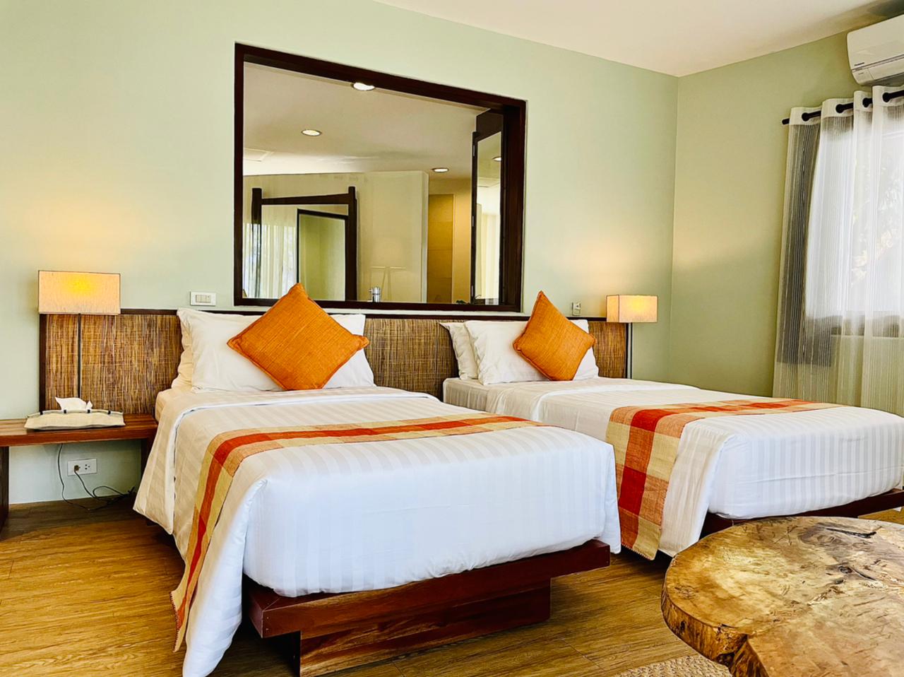 Bright bedroom with two twin beds, orange accents, bedside lamps, and a large wall mirror
