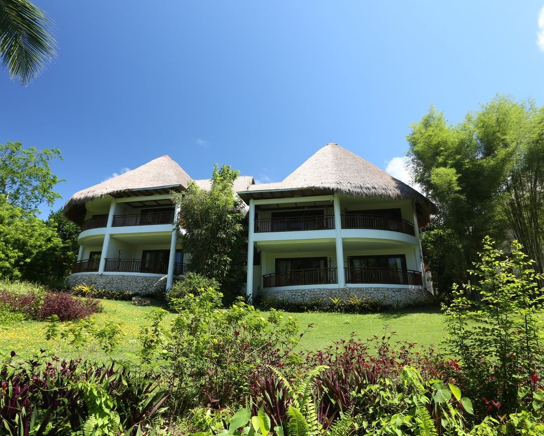 Two thatched-roof tropical villas on a green hillside under a bright blue sky
