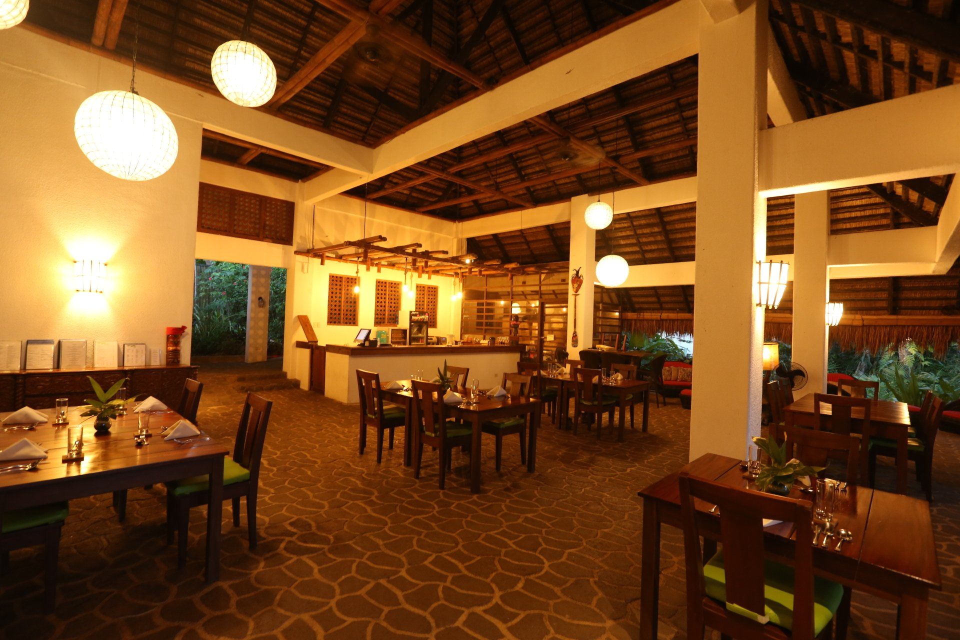 Warm, rustic restaurant interior with wooden tables, hanging globe lights, and high beamed ceiling