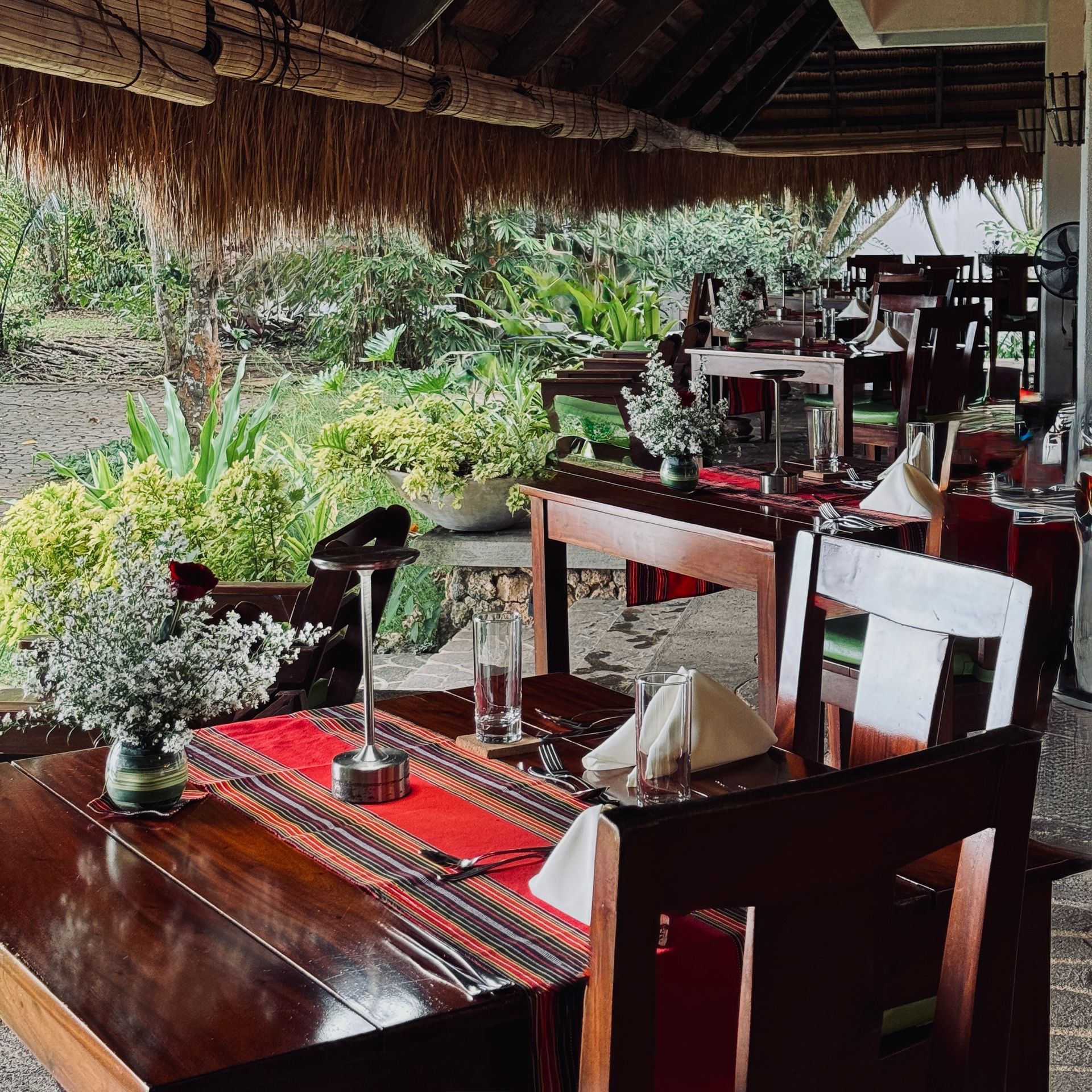 Open-air restaurant tables with red placemats, overlooking a lush tropical garden