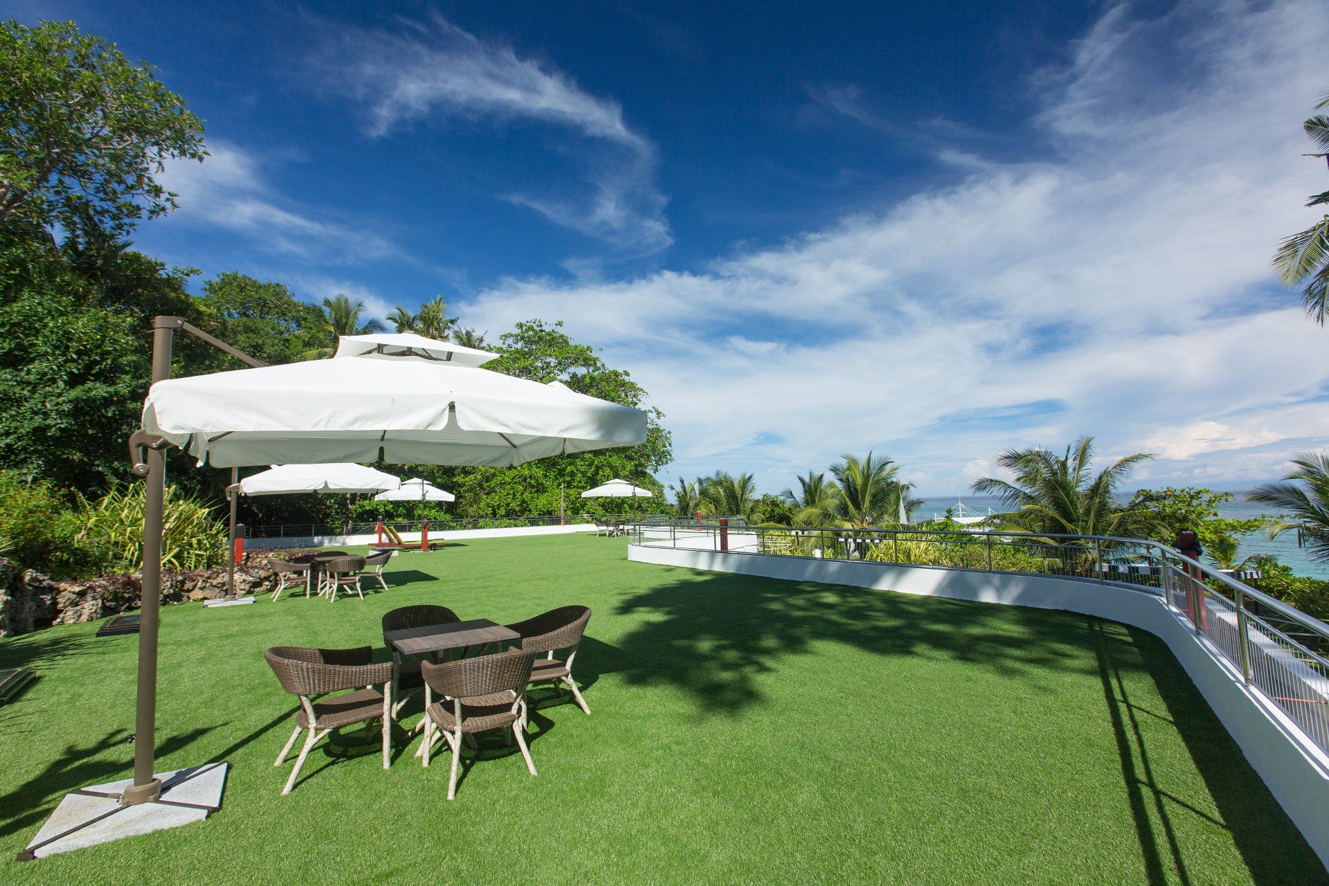 Patio with white umbrella, table and chairs on a green lawn beside a pool under a blue sky