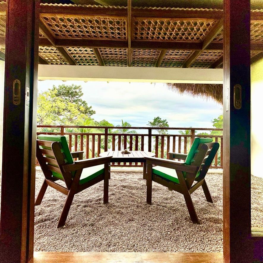 Two green chairs on a porch facing a tropical landscape and ocean view