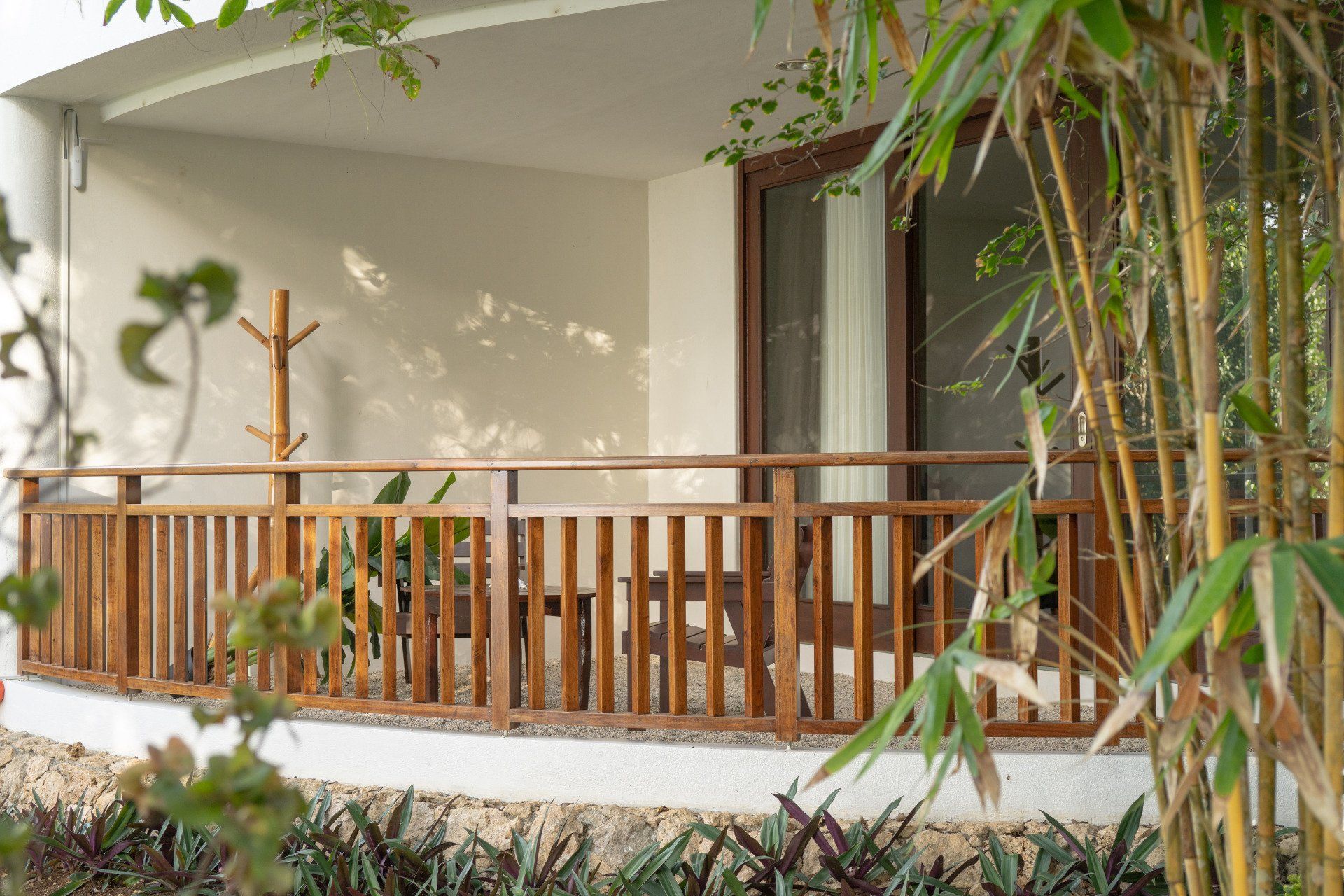 Wooden porch with railings and bamboo plants beside a sliding glass door