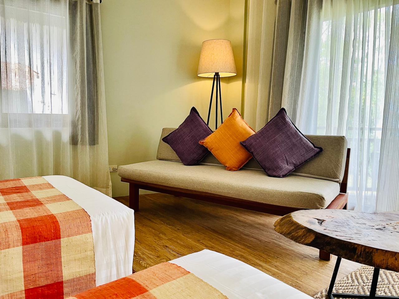 Cozy bedroom with twin beds, colorful pillows, a floor lamp, and sheer curtains by the windows