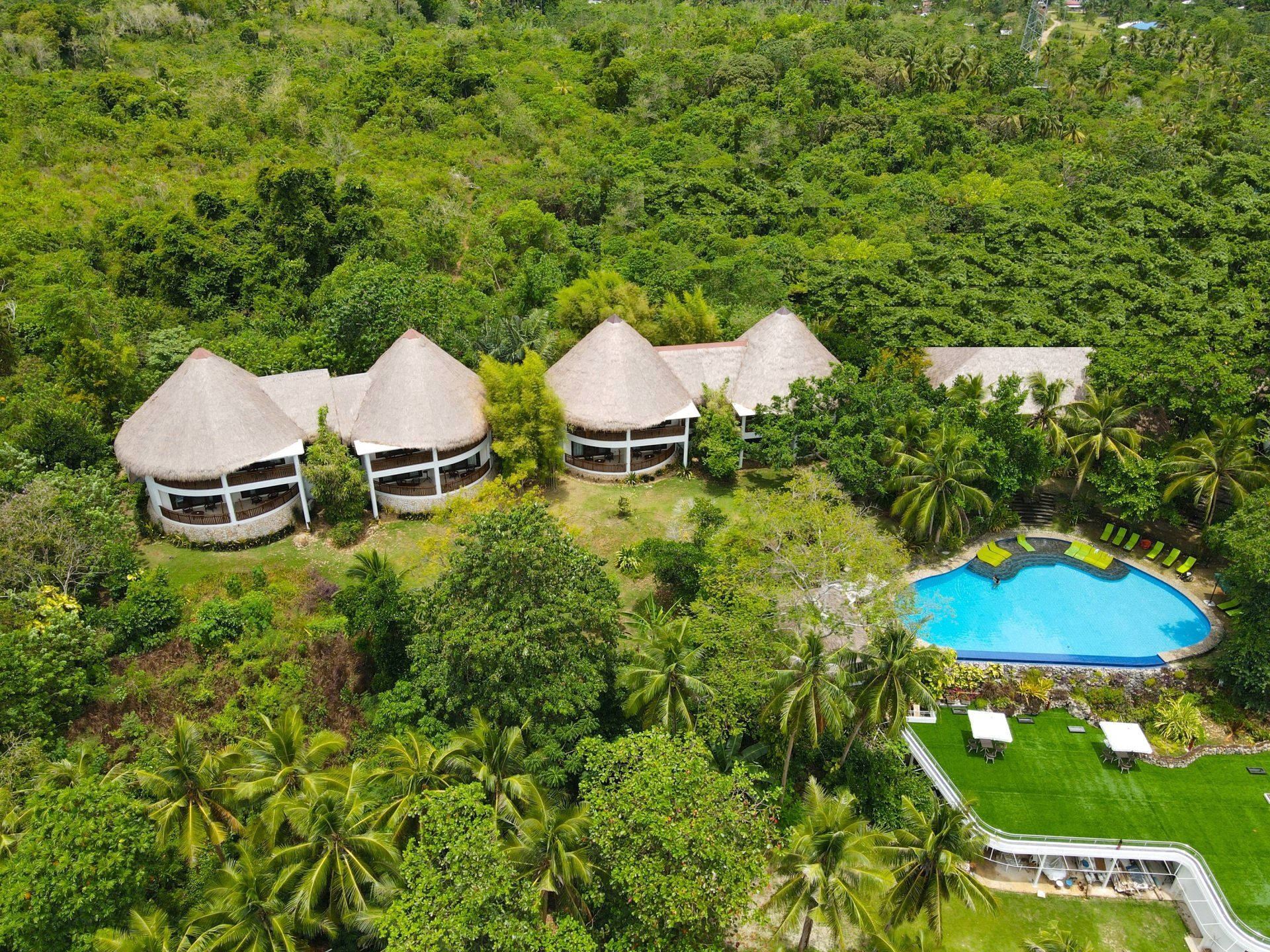 Tropical resort with thatched huts and a blue pool surrounded by lush green trees