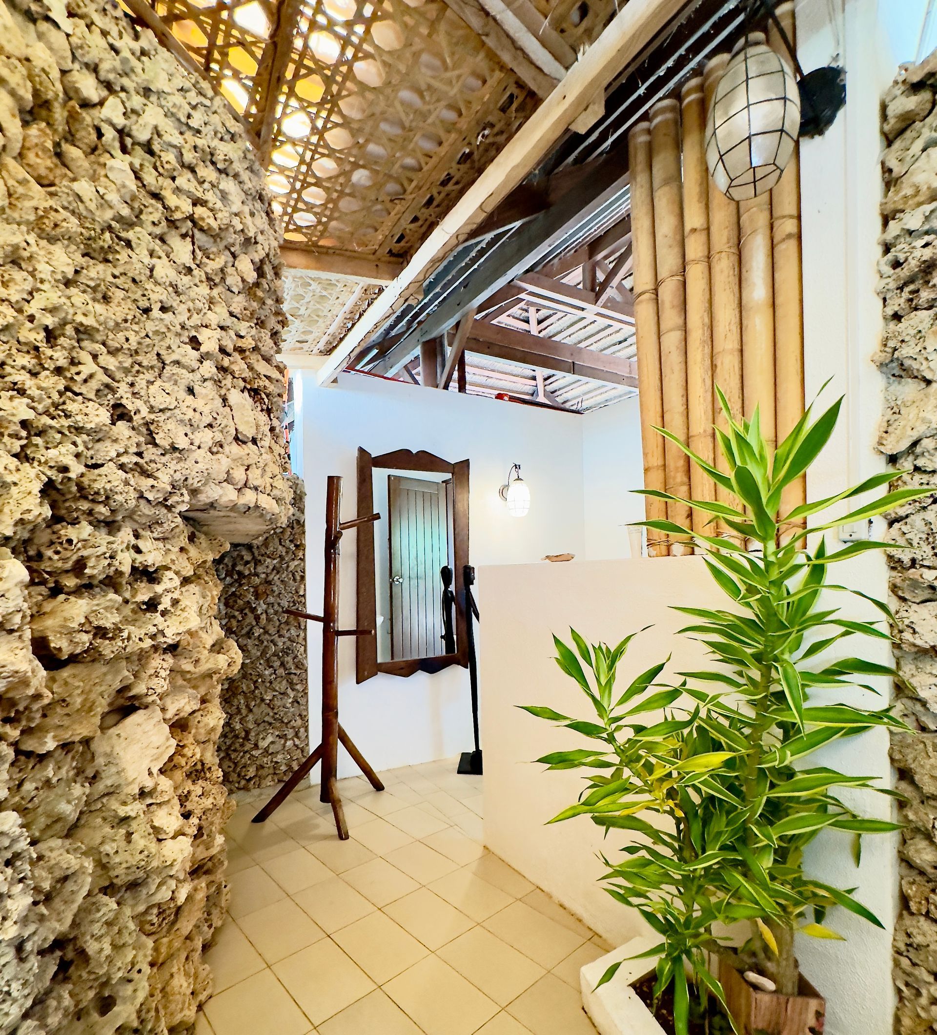 Narrow tropical hallway with stone walls, bamboo ceiling, tiled floor, and a potted plant by a doorway