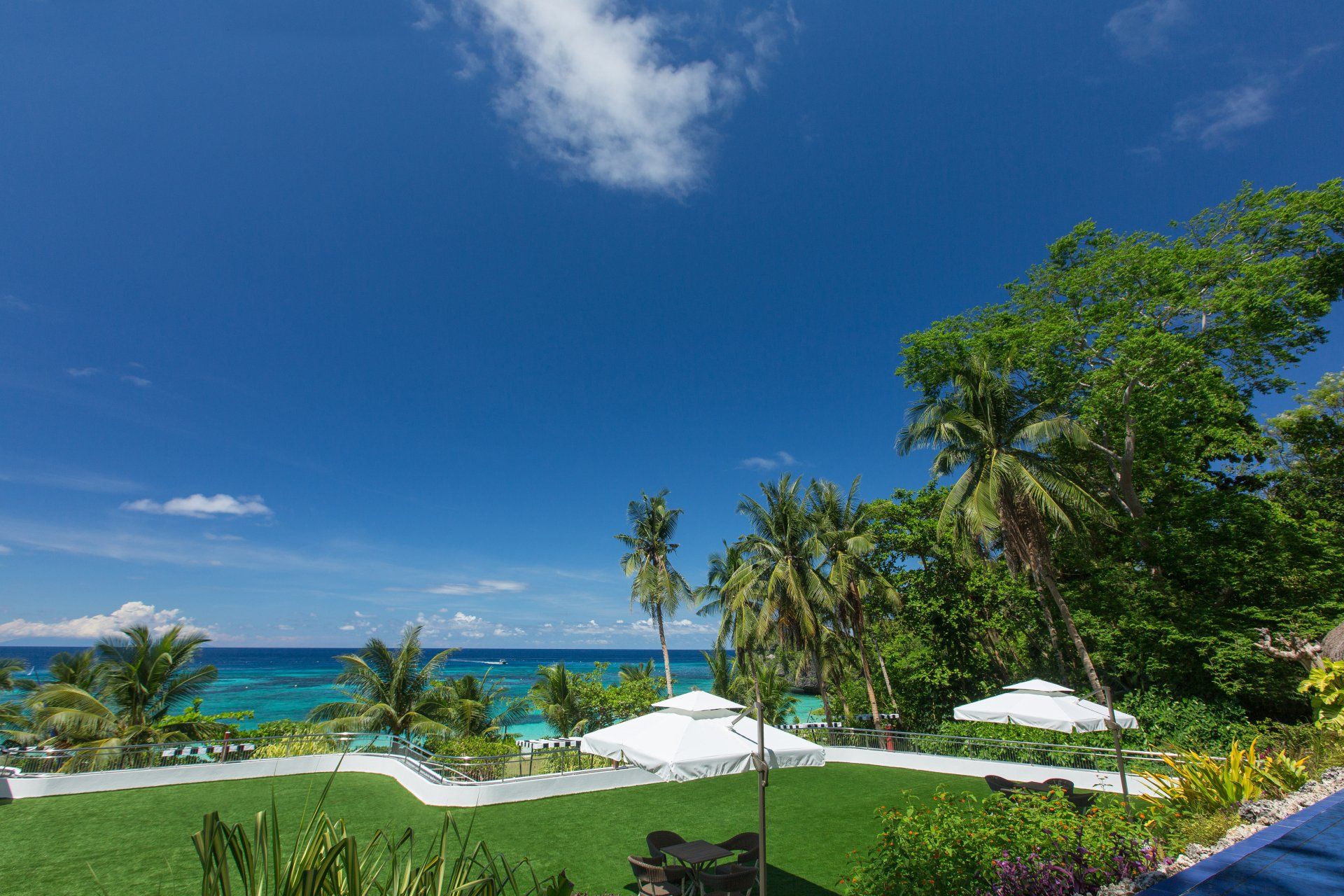 Tropical beach resort with turquoise ocean, palm trees, and white umbrellas under a clear blue sky