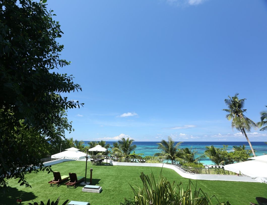 Tropical resort lawn with white umbrellas, lounge chairs, palm trees, and turquoise ocean under a clear blue sky