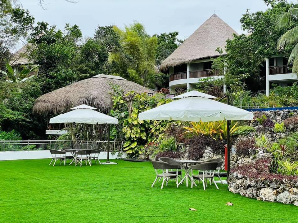 Lush garden resort with white umbrellas, tables, and a thatched-roof building