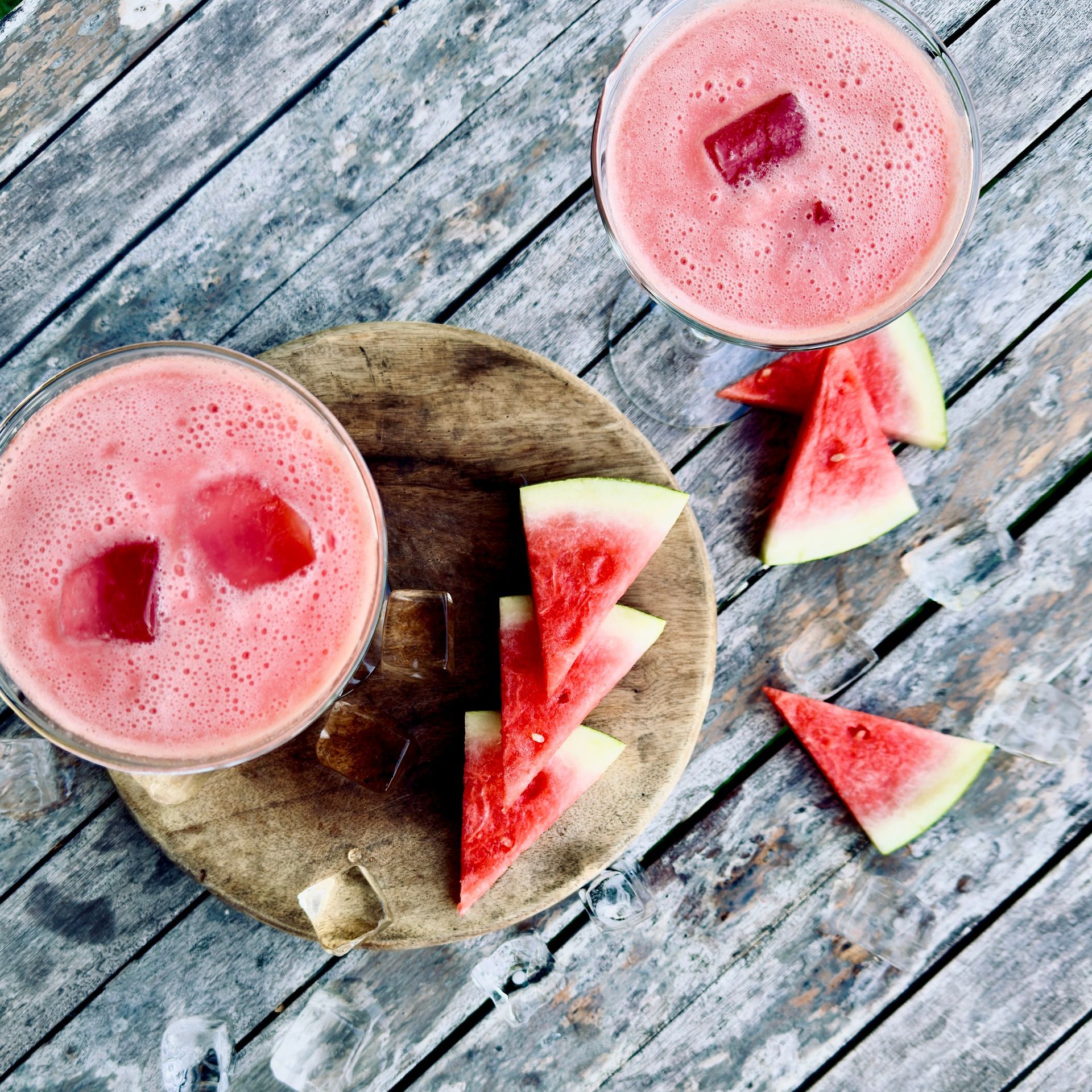 Two pink watermelon smoothies with watermelon slices on a rustic wooden table
