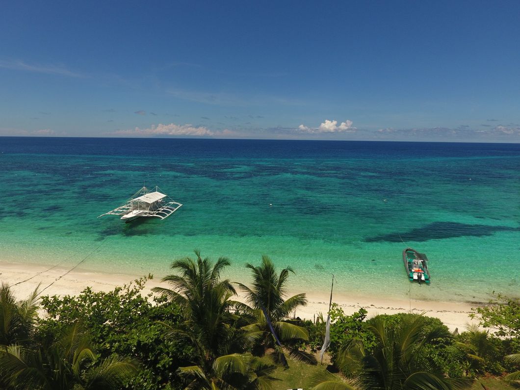 Tropical beach with turquoise water, a white boat offshore, and palm trees in the foreground