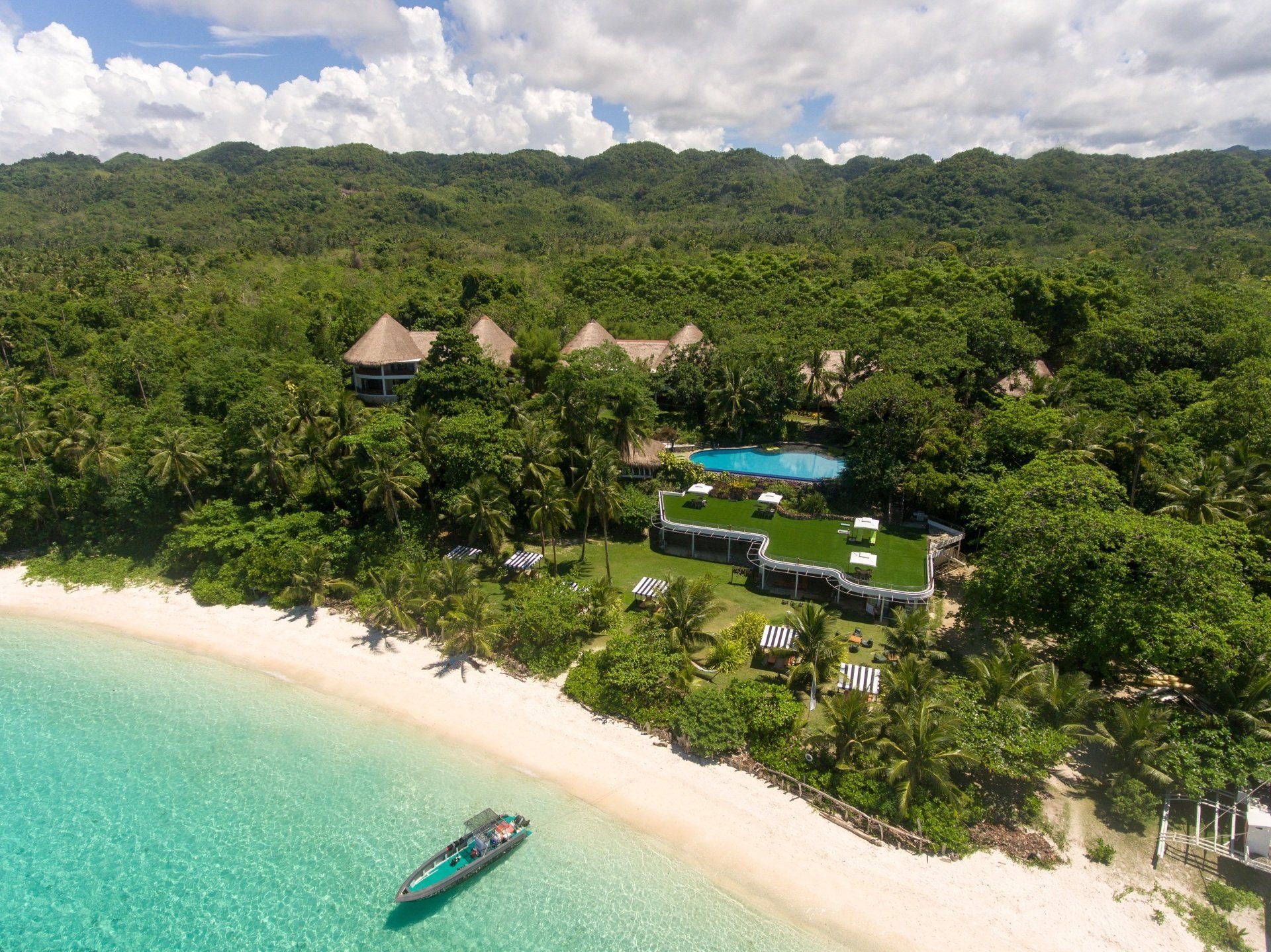 Aerial view of a tropical beach resort with turquoise water, white sand, palm trees, and villas