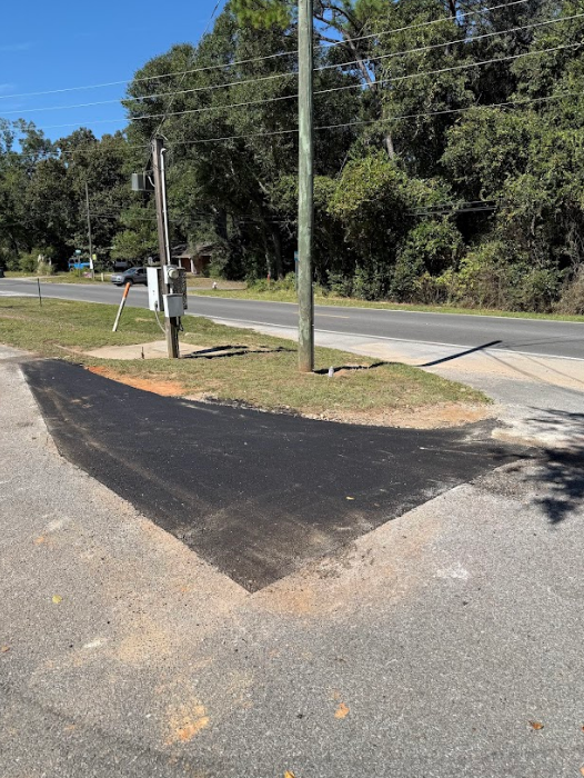 Newly paved asphalt area adjacent to a roadway and utility pole.