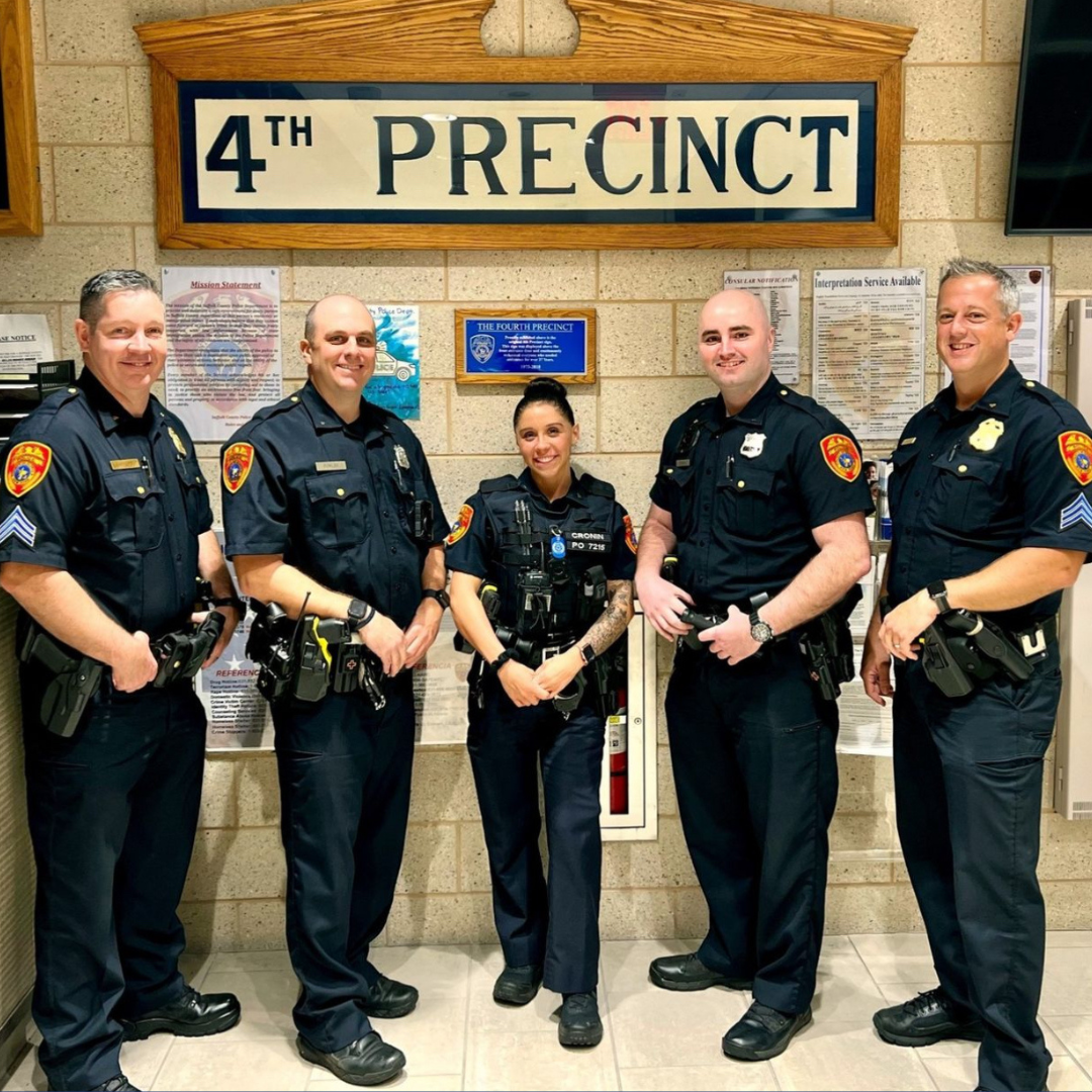 A group of police officers are posing for a picture under a sign that says 4th precinct