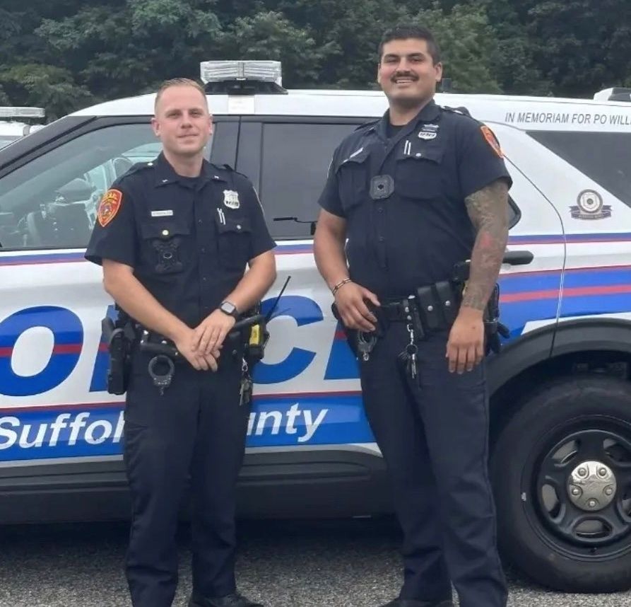 Two police officers standing in front of a suffolk county police car