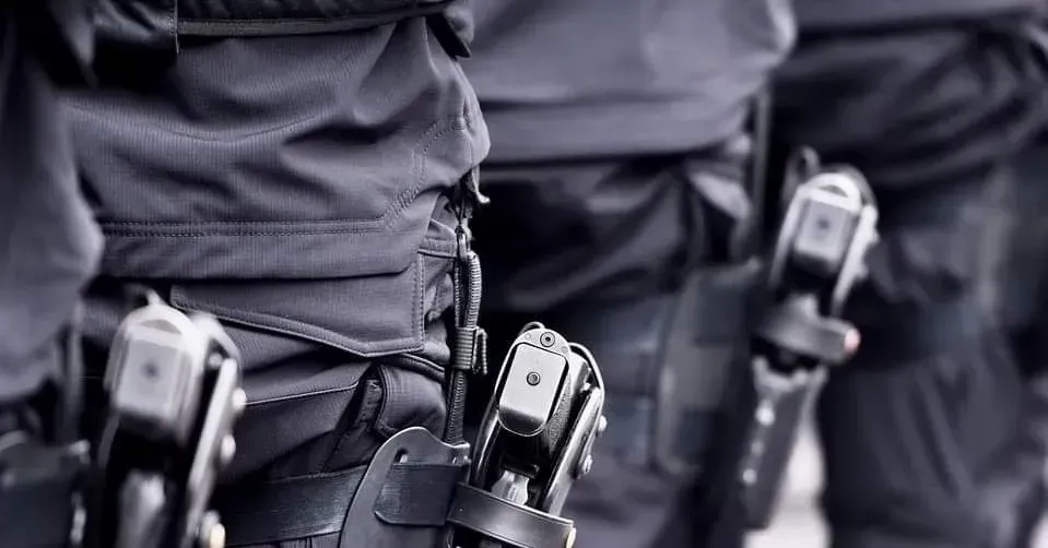 Uniformed personnel in black tactical gear with holstered sidearms worn on their belts.
