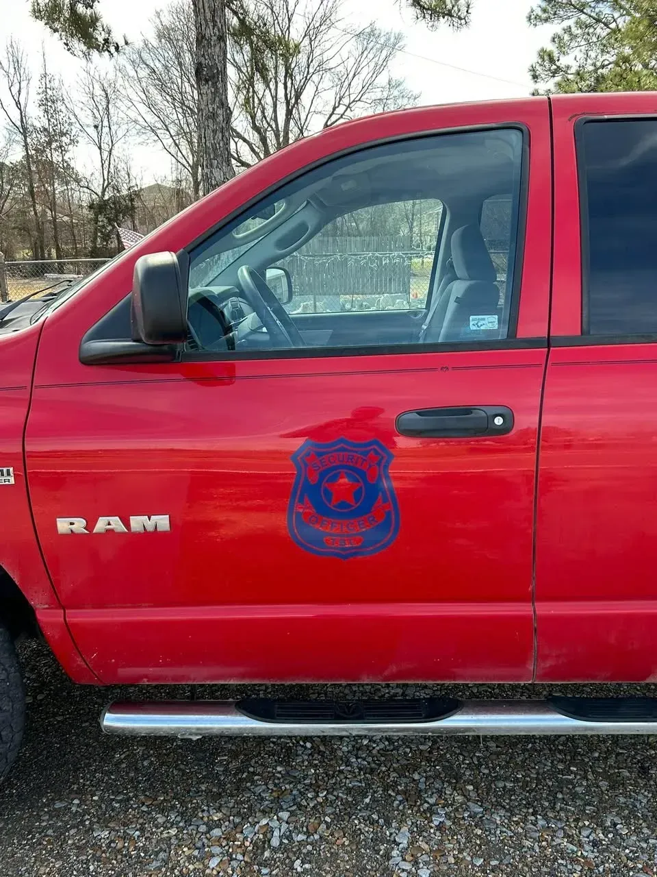 A red RAM pickup truck with a blue law enforcement-style badge decal on the driver-side door.