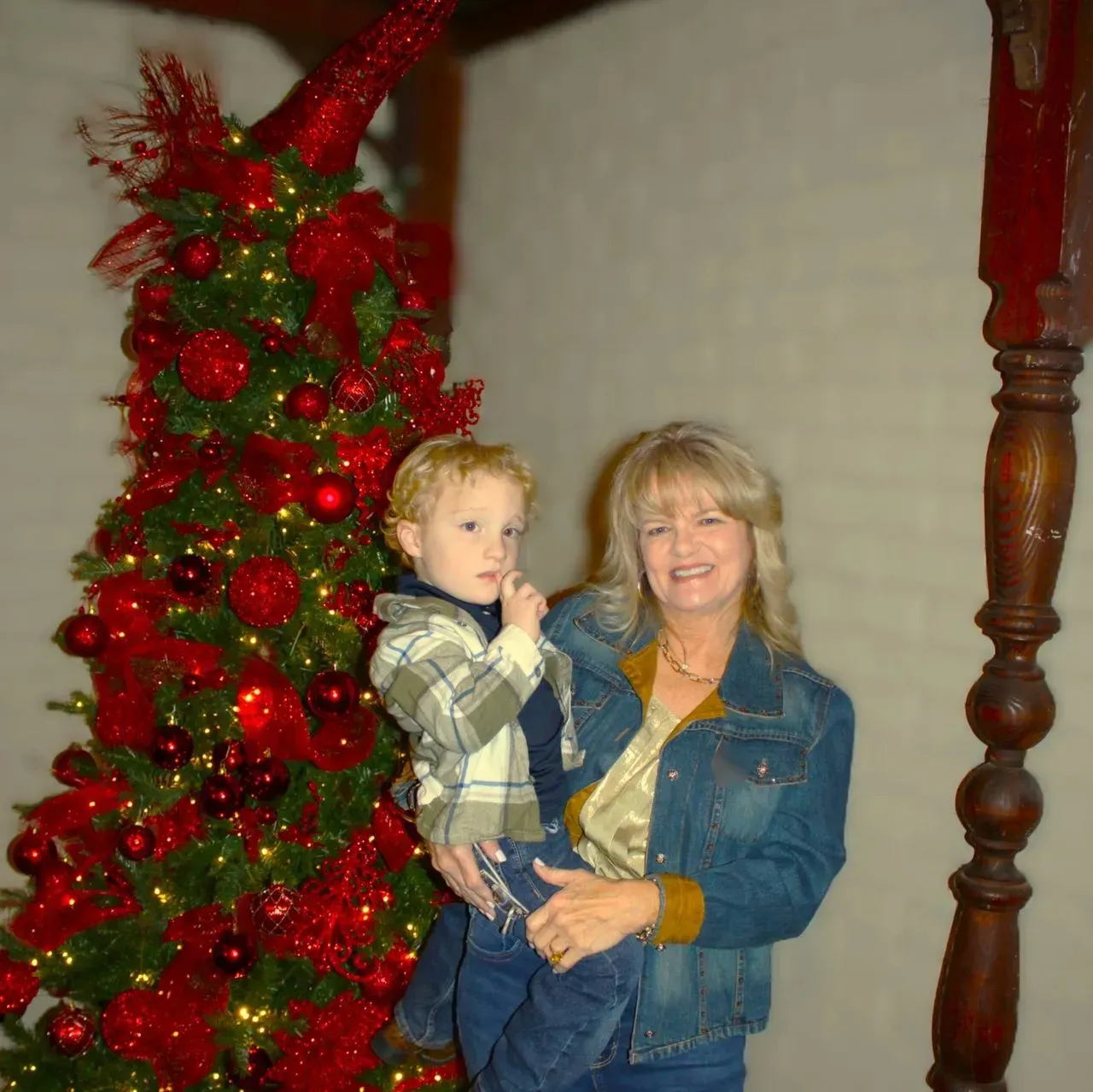 A person holding a child next to a tall, decorated Christmas tree adorned with bright red ornaments and lights.