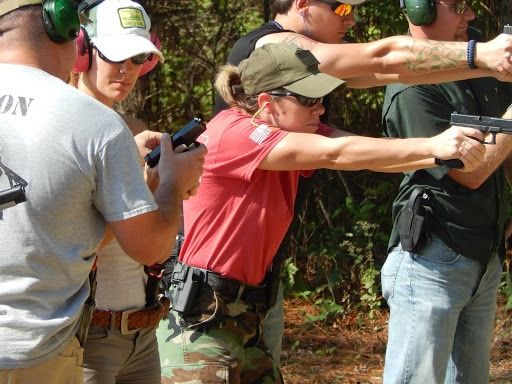 A group of people standing on an outdoor range while practicing shooting handguns.