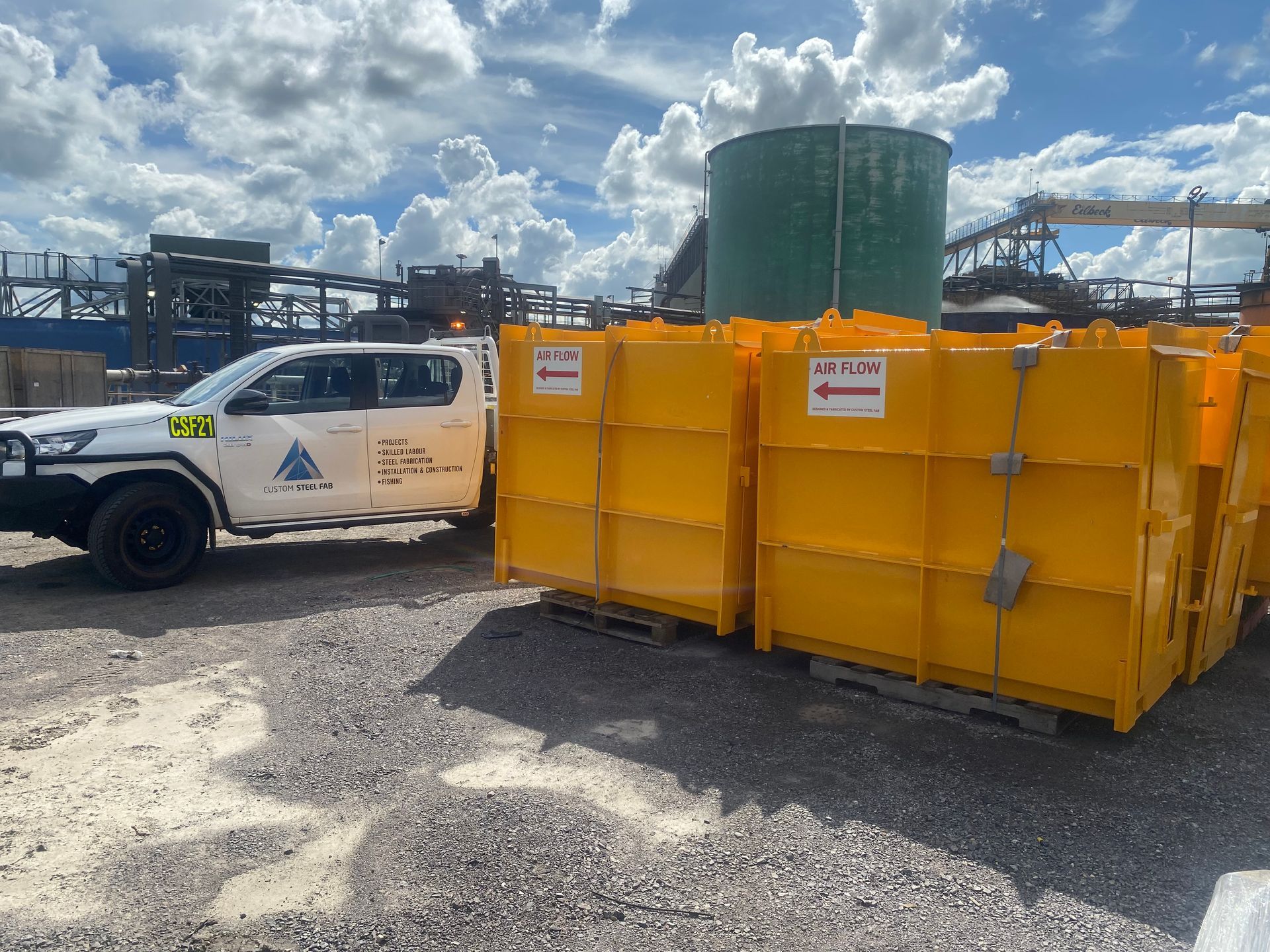 Construction site with white utility truck and bright yellow dumpsters under a cloudy sky — Vent Doors Australia in Ryan, QLD