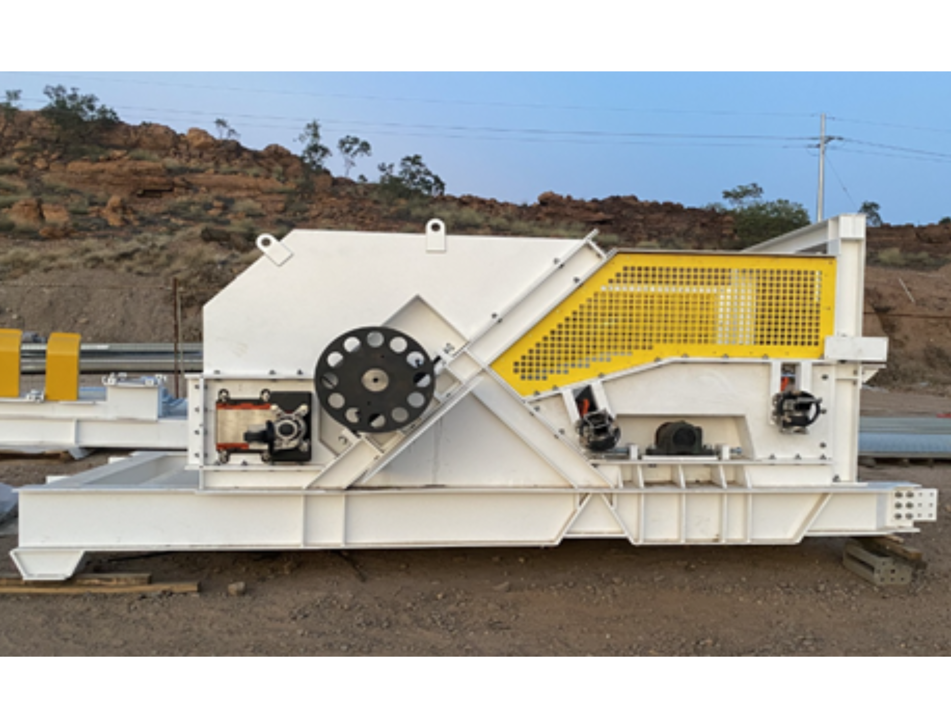 White industrial crusher machine with yellow guard panels on a gravel lot