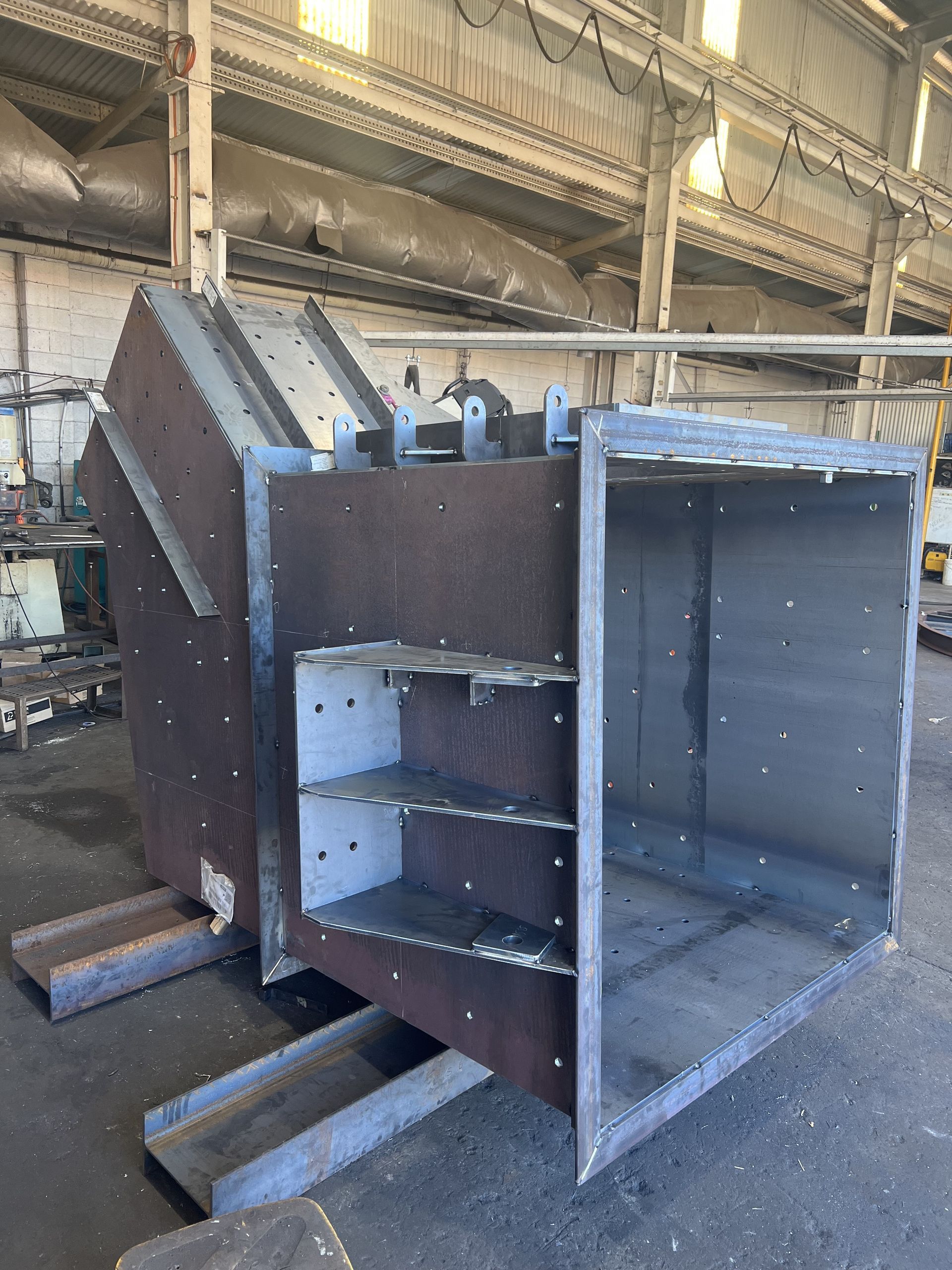 Large industrial metal duct or hopper with open rectangular end, in a factory workshop, showing internal shelves — Vent Doors Australia in Ryan, QLD