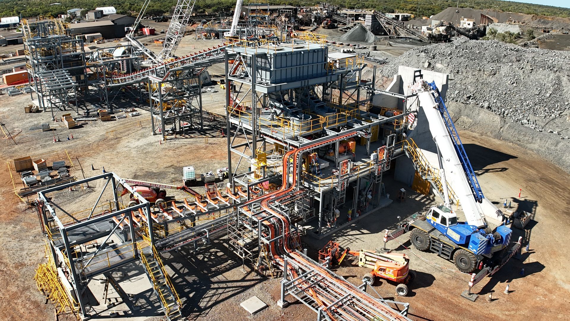 Aerial view of a construction site with steel framework, machinery, and a large white crane truck on dirt ground