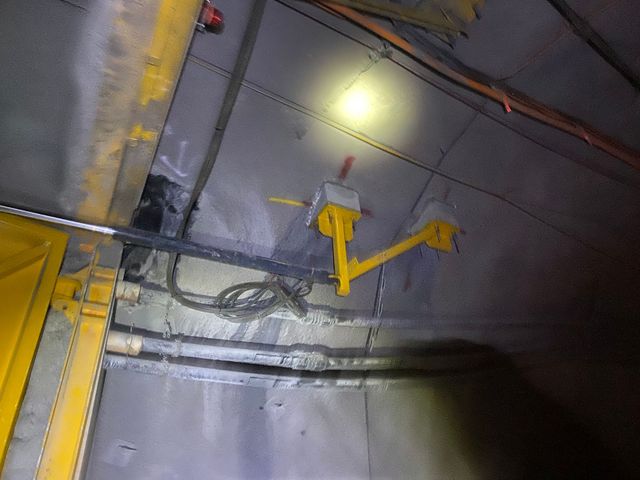 Dim industrial ceiling with yellow pipes, wiring, and a bright overhead light — Vent Doors Australia in Bohle, QLD