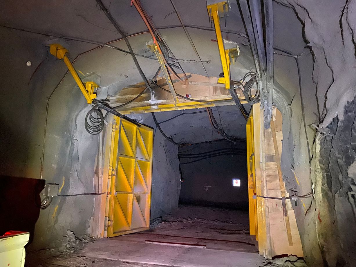 Yellow industrial doors in a rocky tunnel entrance with overhead cables and dim lighting