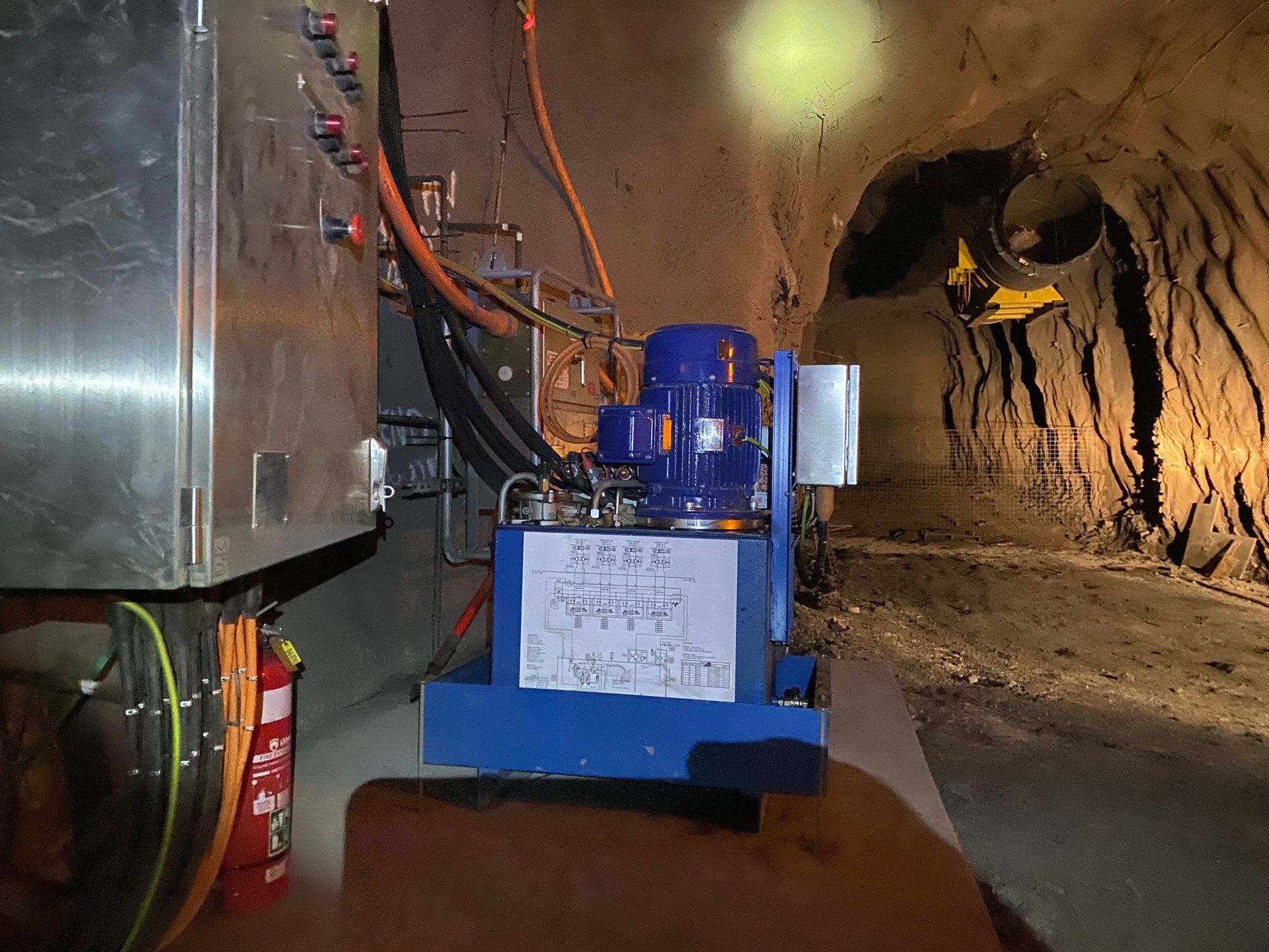 Blue mining machine in a tunnel with hoses, lights, and a rocky underground wall — Vent Doors Australia in Bohle, QLD