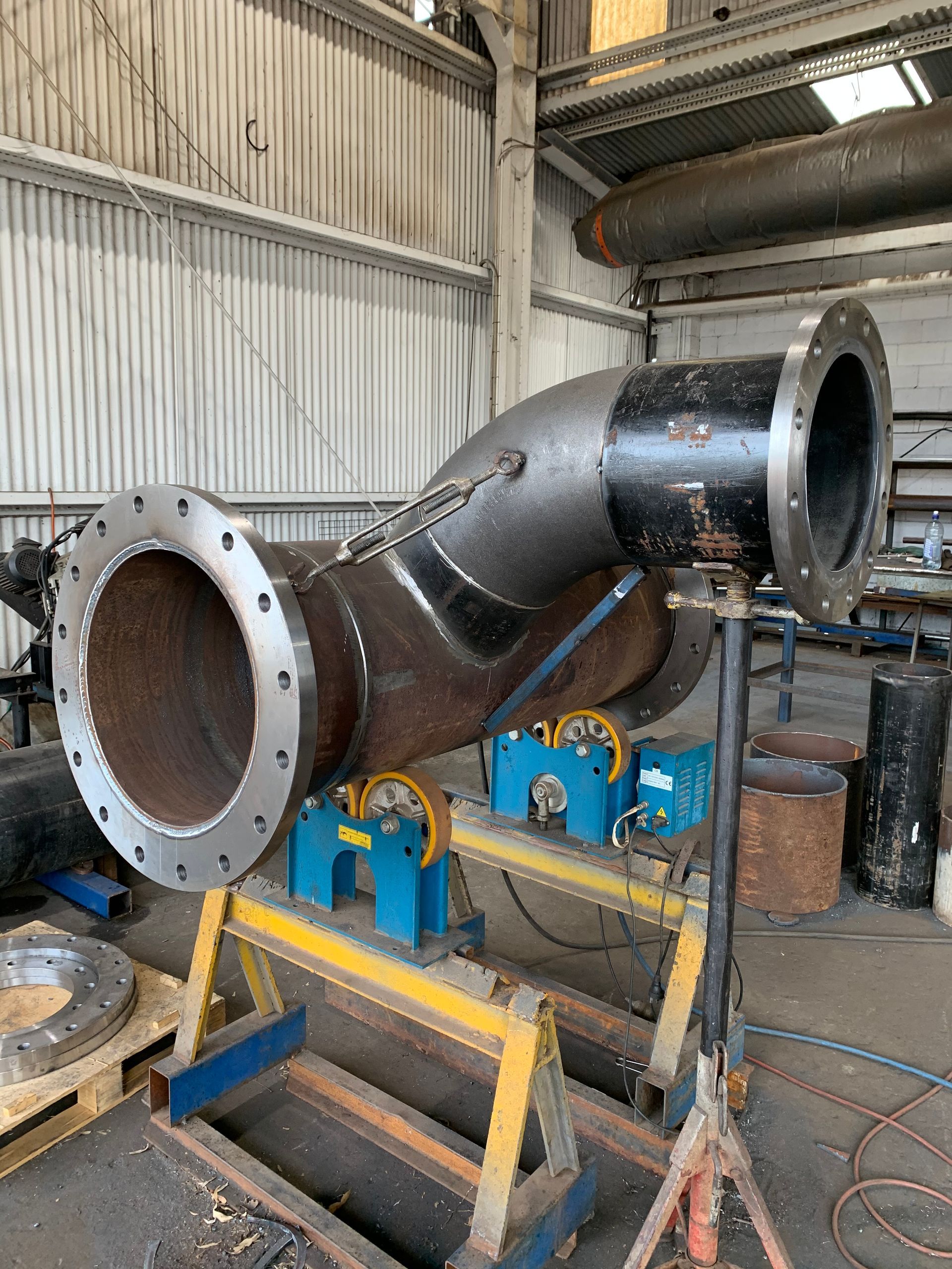 Large black industrial pipe section mounted on blue and yellow machinery in a workshop — Vent Doors Australia in Ryan, QLD
