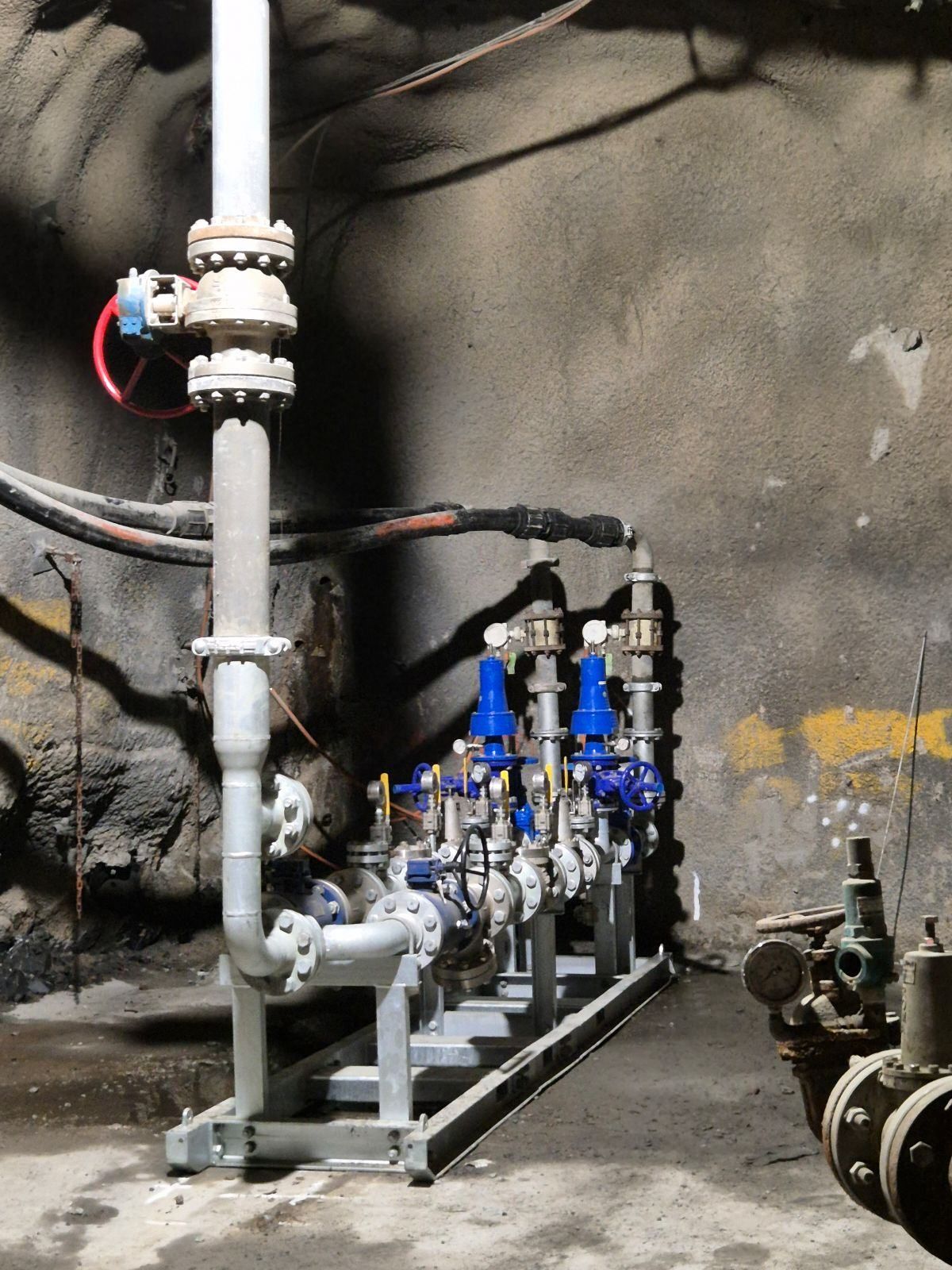 Industrial pipes and blue valves on a metal frame in a dim utility room