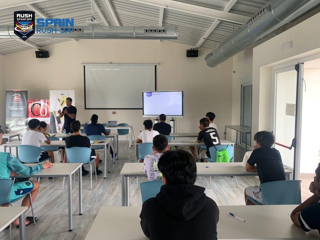 Indoor classroom with students seated at desks facing a front projector and display screens
