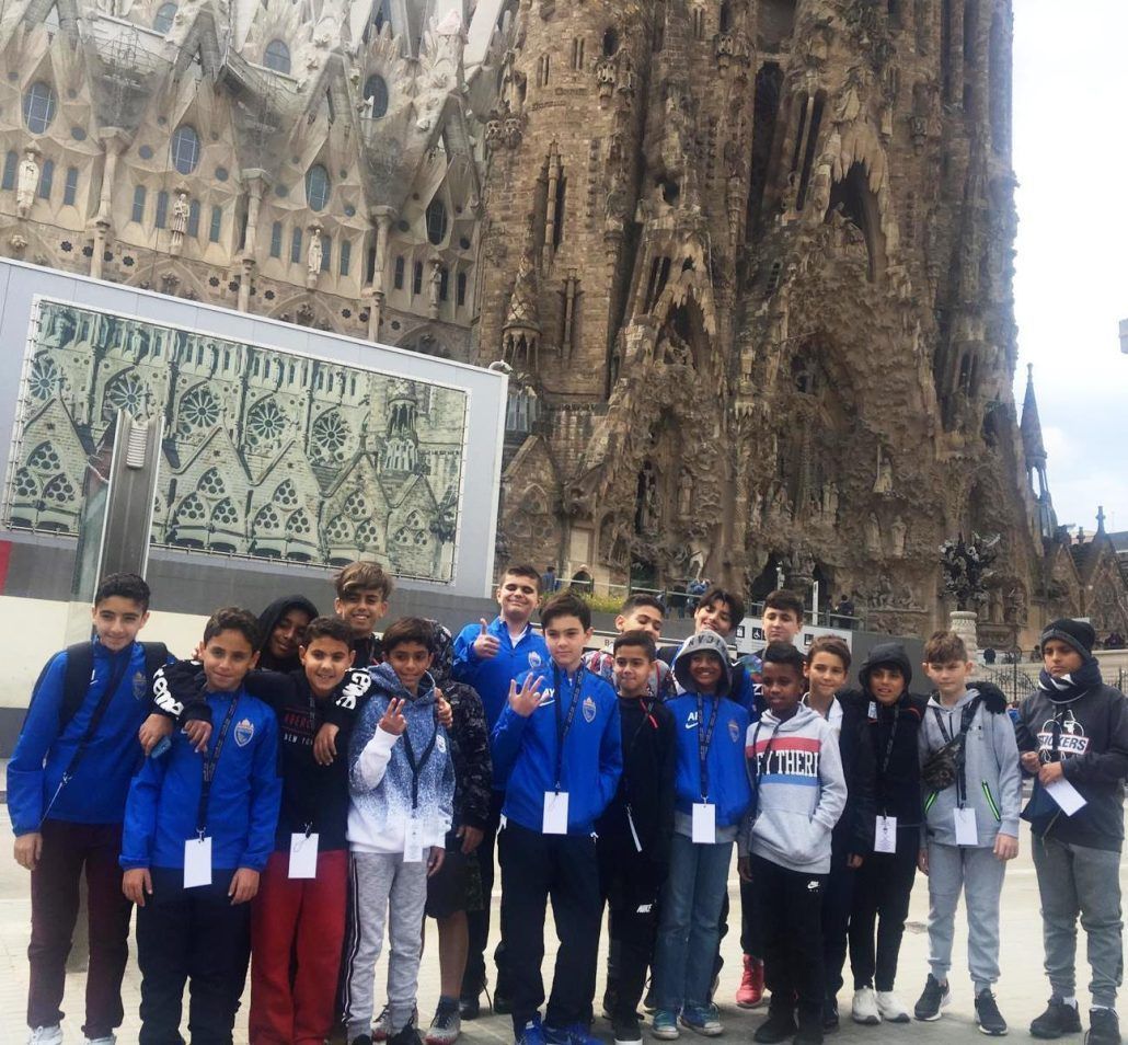 Group of people in blue jackets posing in front of a cathedral facade and ornate stone wall.