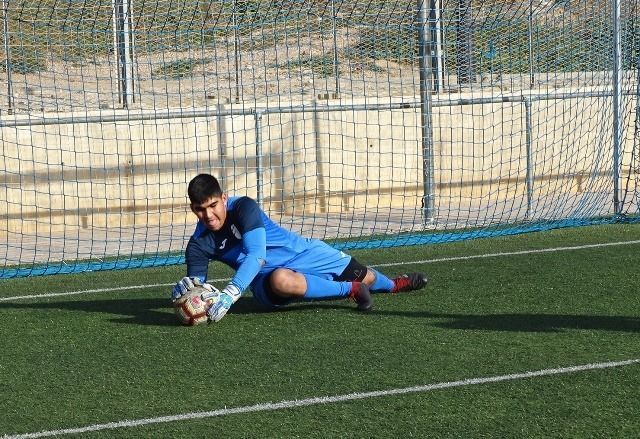 Soccer goalkeeper in blue diving low to save the ball on a field near the goal line