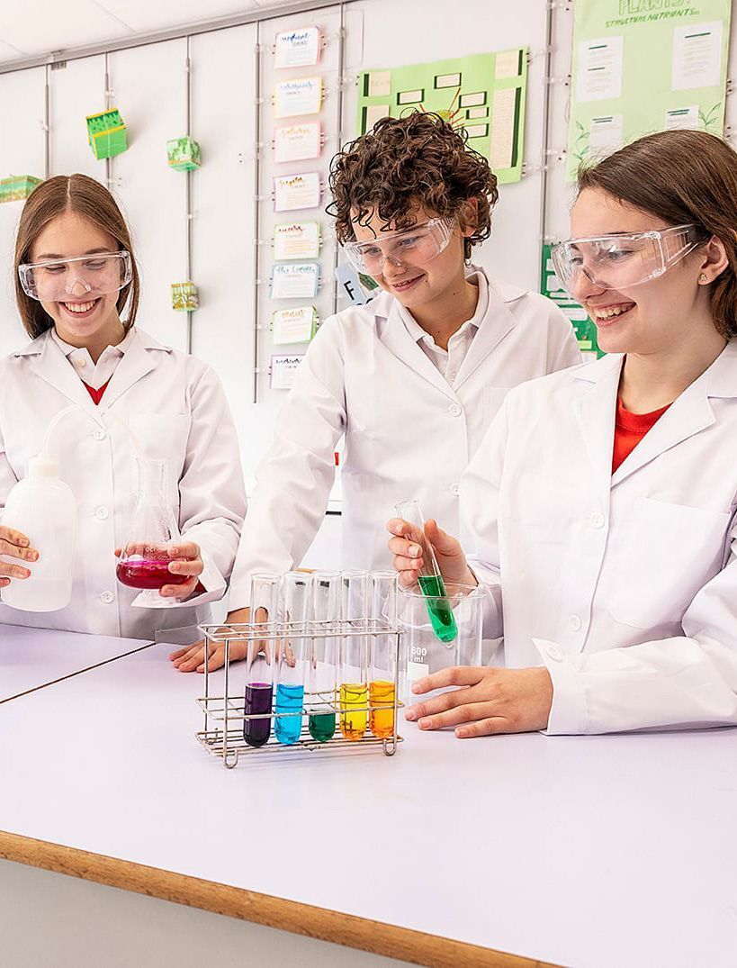 Students in white lab coats work with colorful liquids in a science classroom laboratory.