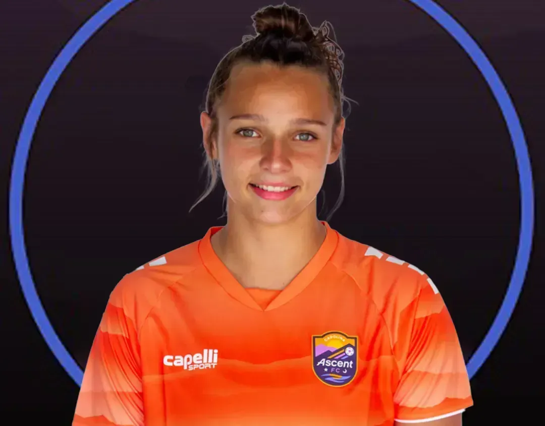 Female soccer player in orange jersey, smiling against a dark background with a blue ring