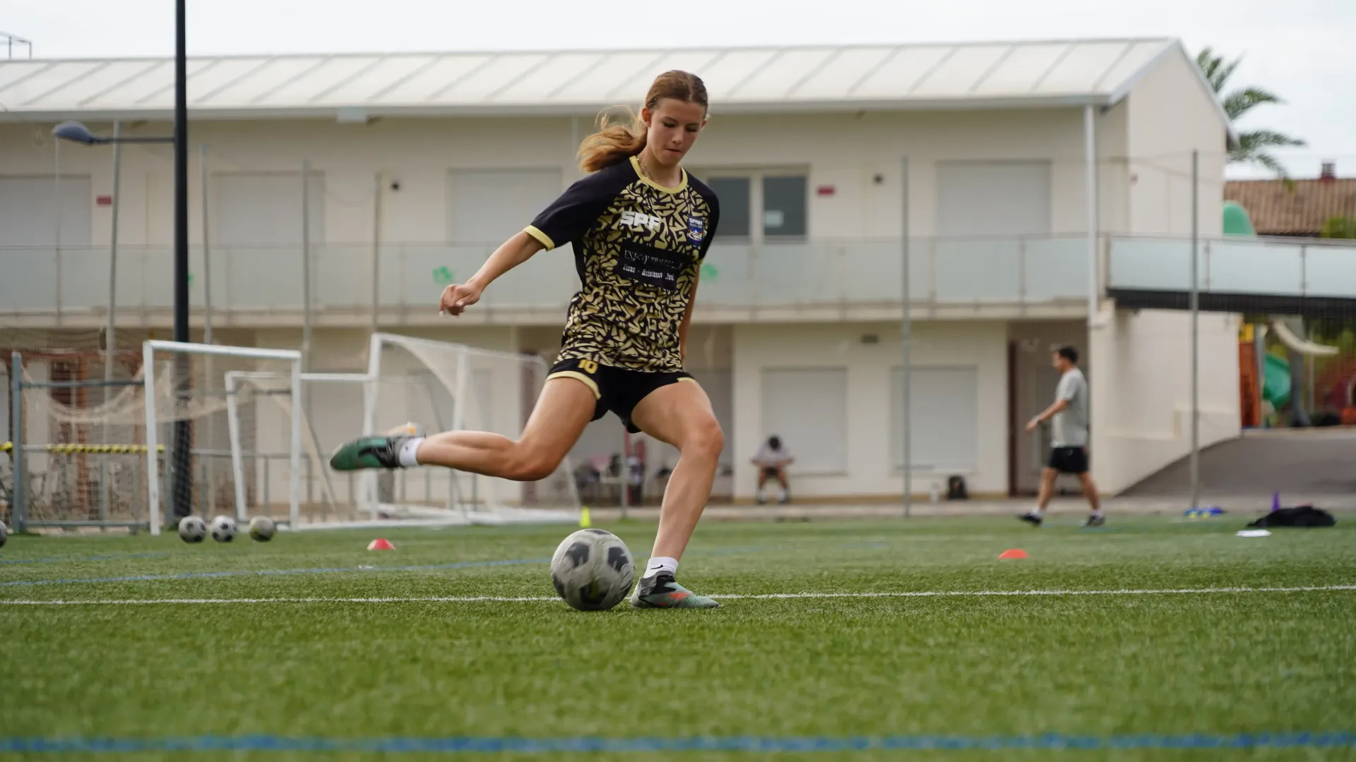 Soccer player in black and gold uniform kicking a ball on a grassy field