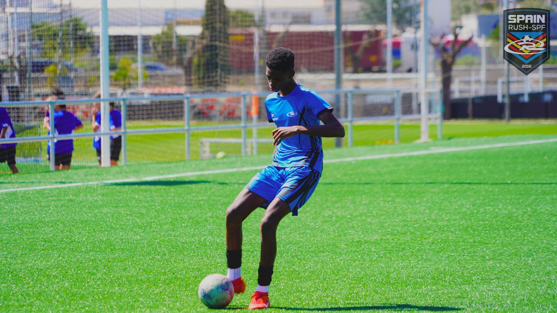 Soccer player in blue controls a ball on a green field near the goal