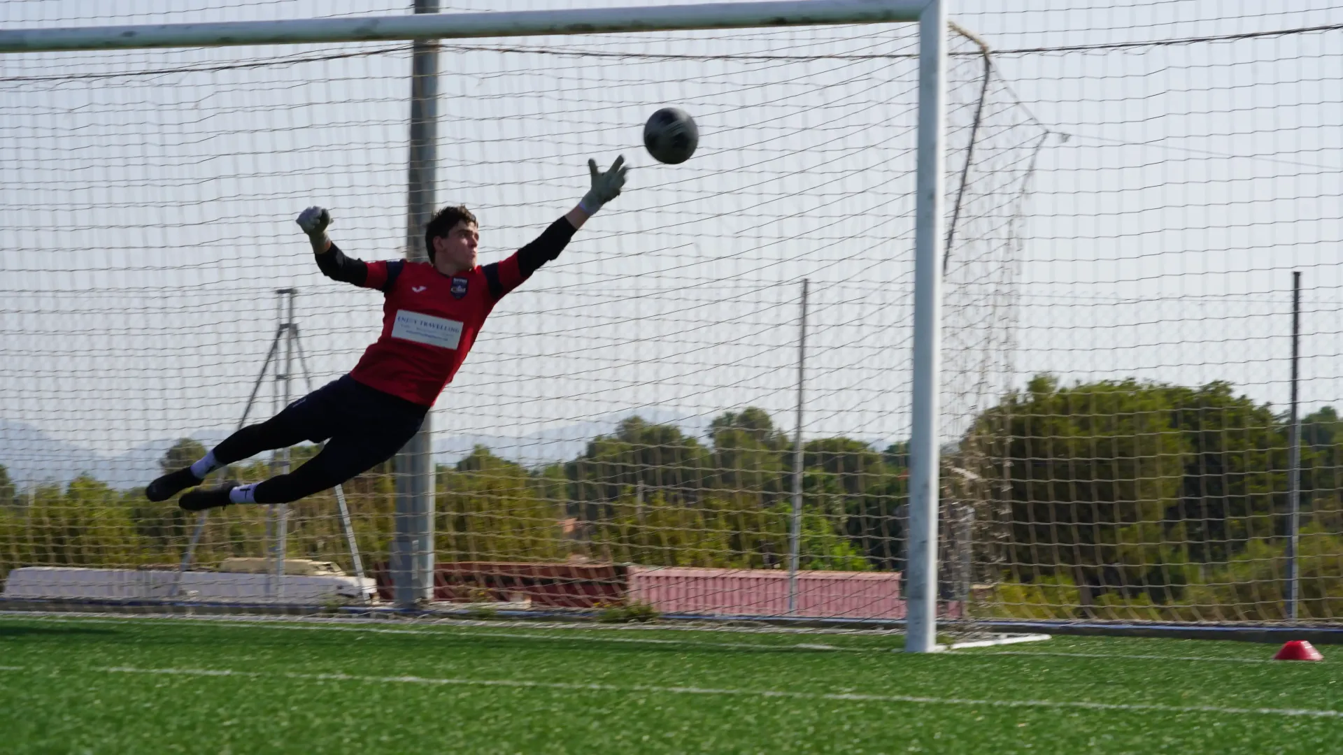 Soccer goalkeeper diving left to block a ball in front of the goal net