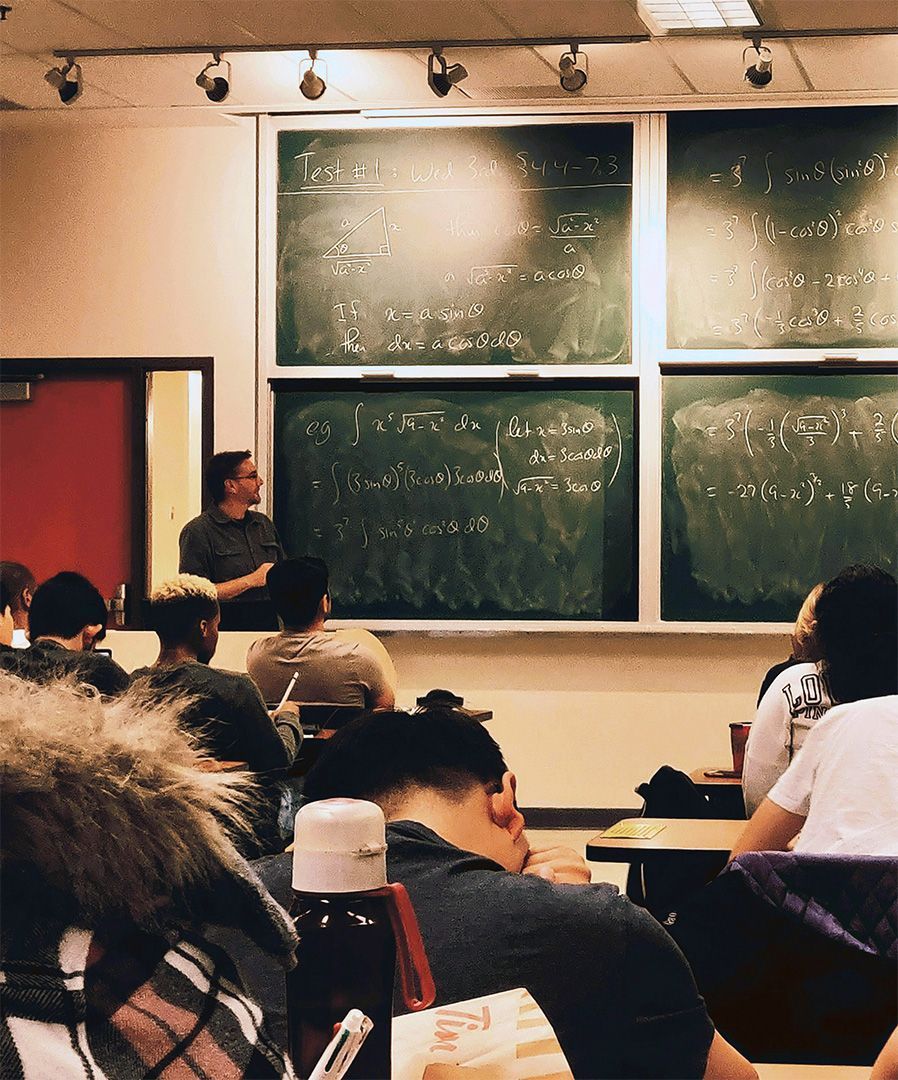 Classroom lecture with students seated before large chalkboards covered in writing