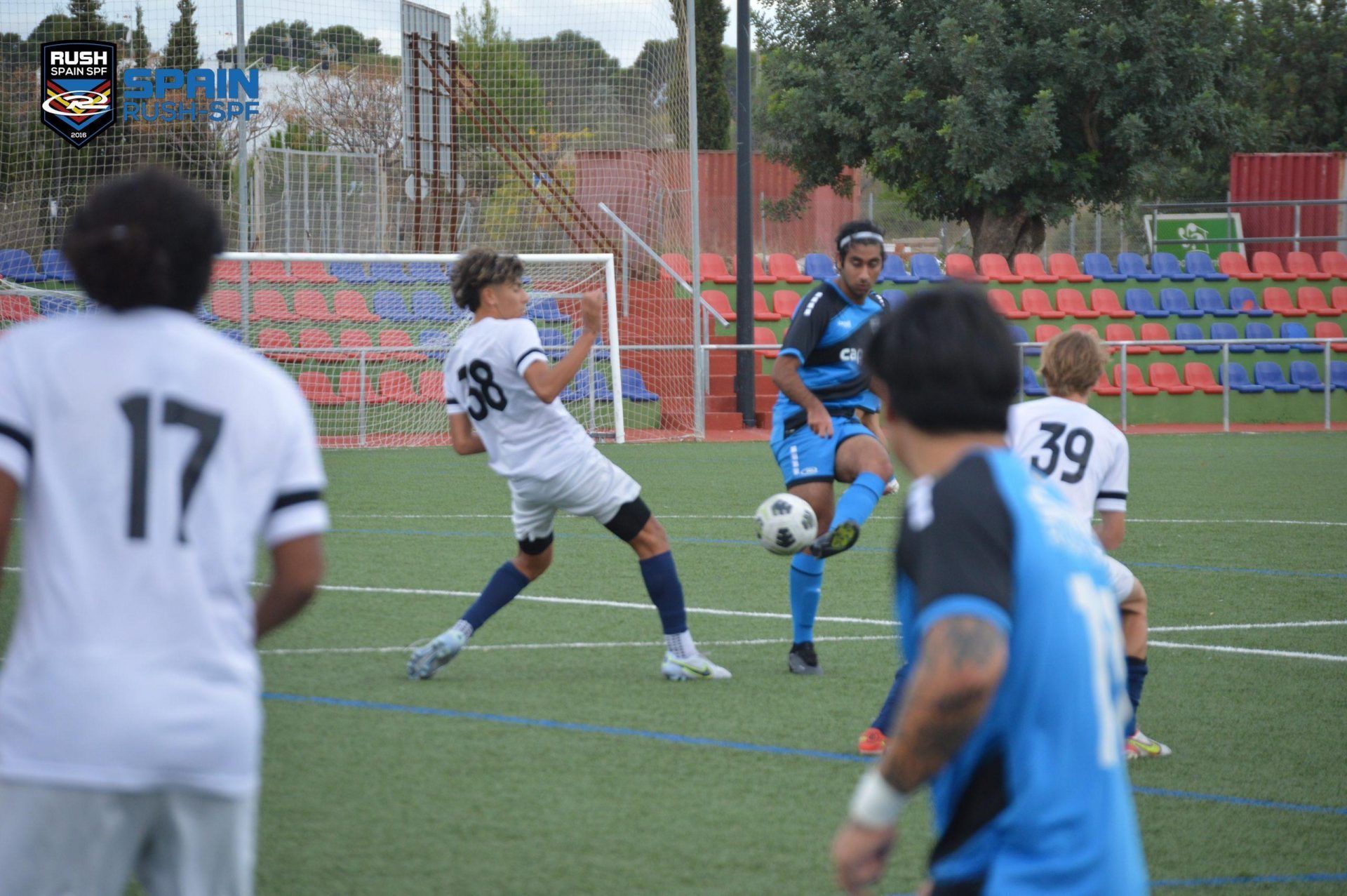 Soccer players in white and blue jerseys contest the ball on a field during a match.
